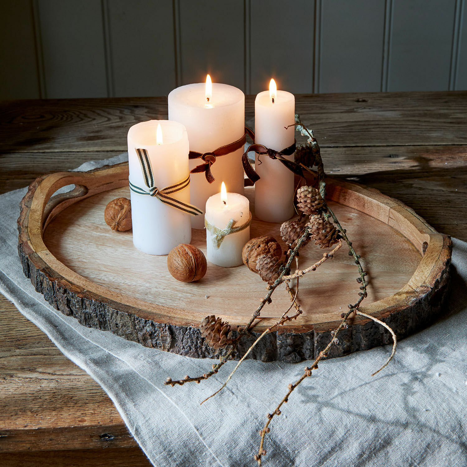 Bandeja Danice Bandeja de madera con corteza natural, cuatro velas blancas encendidas y decoración con nueces y piñas
