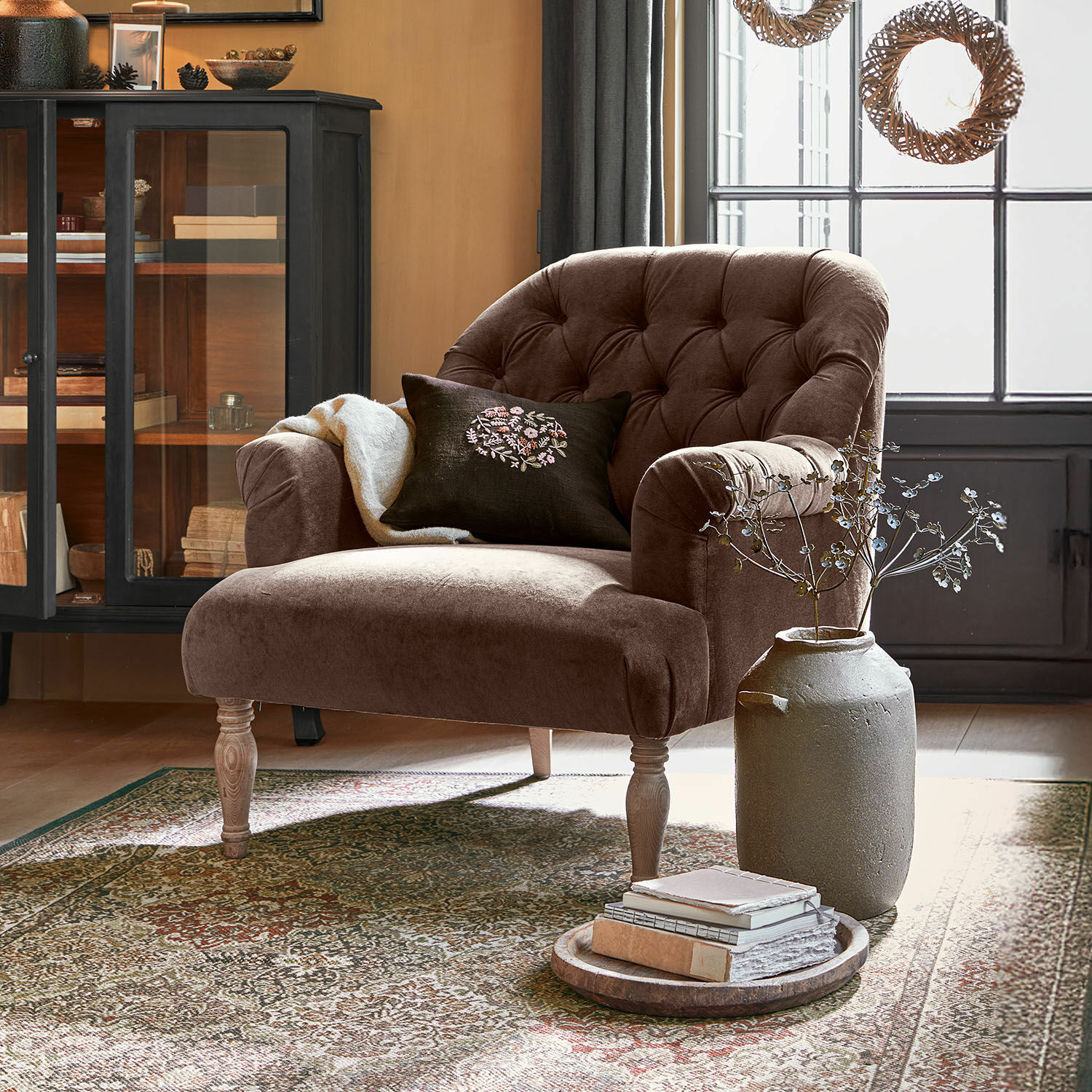 Sillón Shambrook Sillón de terciopelo marrón con respaldo capitoné y patas de madera en salón acogedor con alfombra
