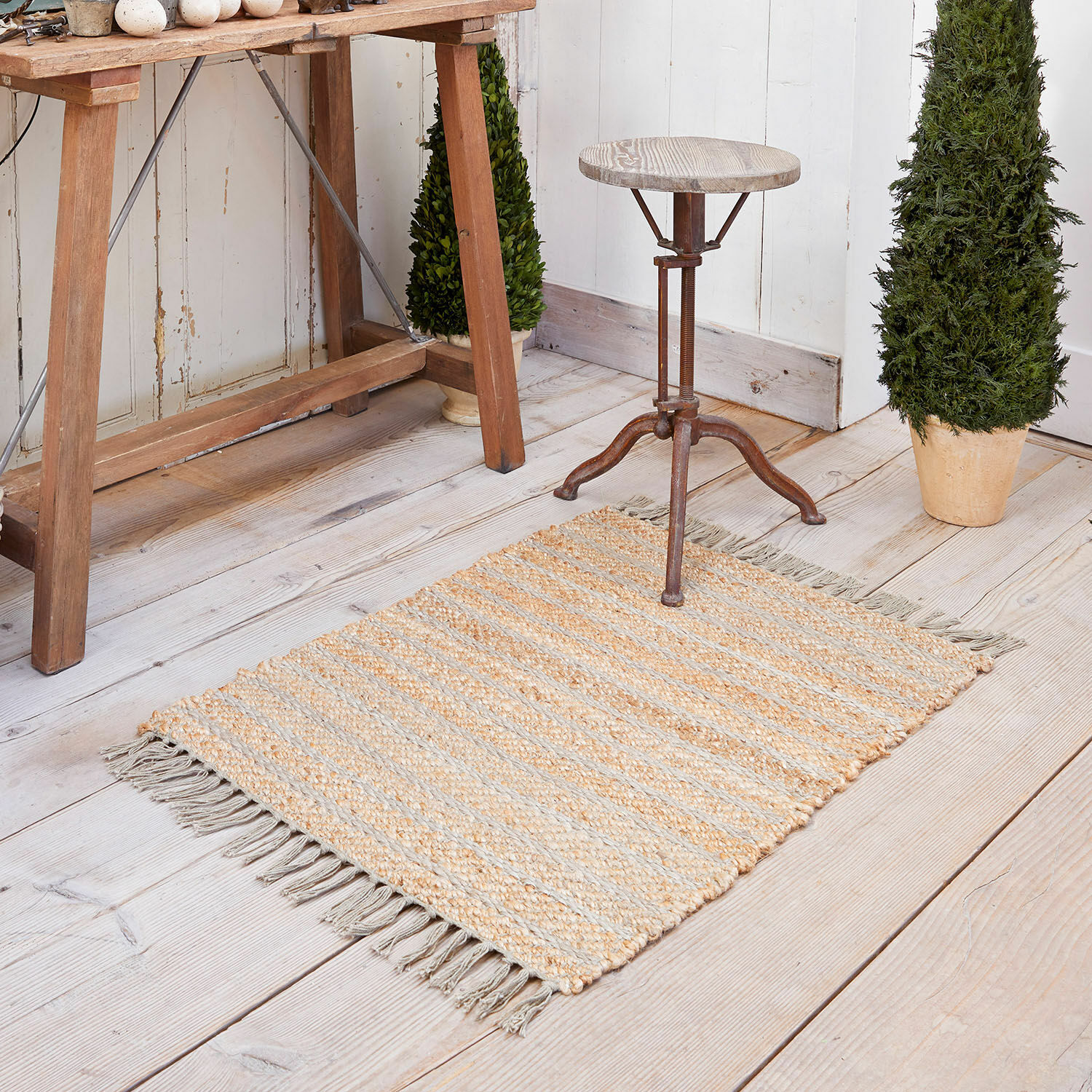 Alfombra Voyage Alfombra de yute beige y gris con rayas y flecos sobre suelo de madera clara, decoración interior