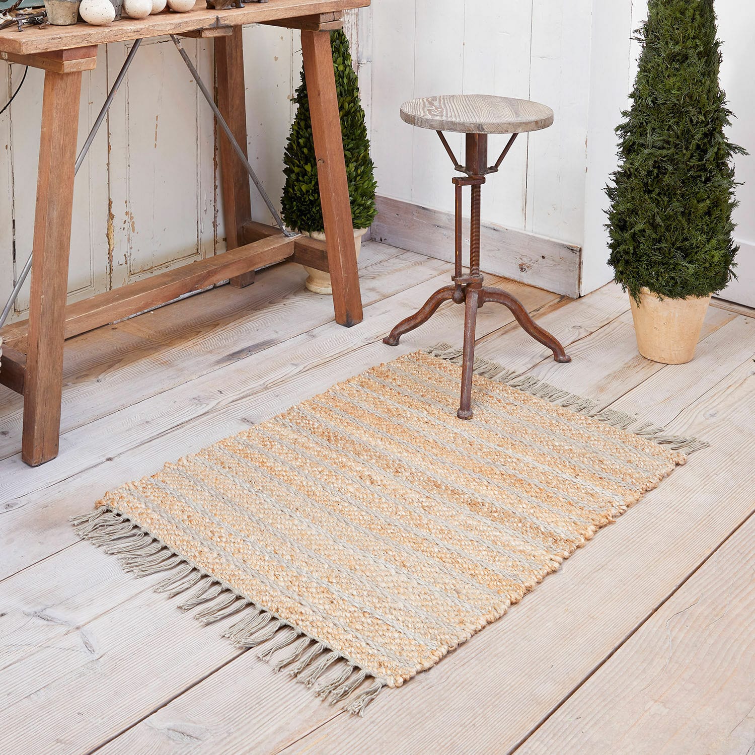 Alfombra Voyage Alfombra de yute beige y gris con rayas y flecos sobre suelo de madera clara, decoración interior