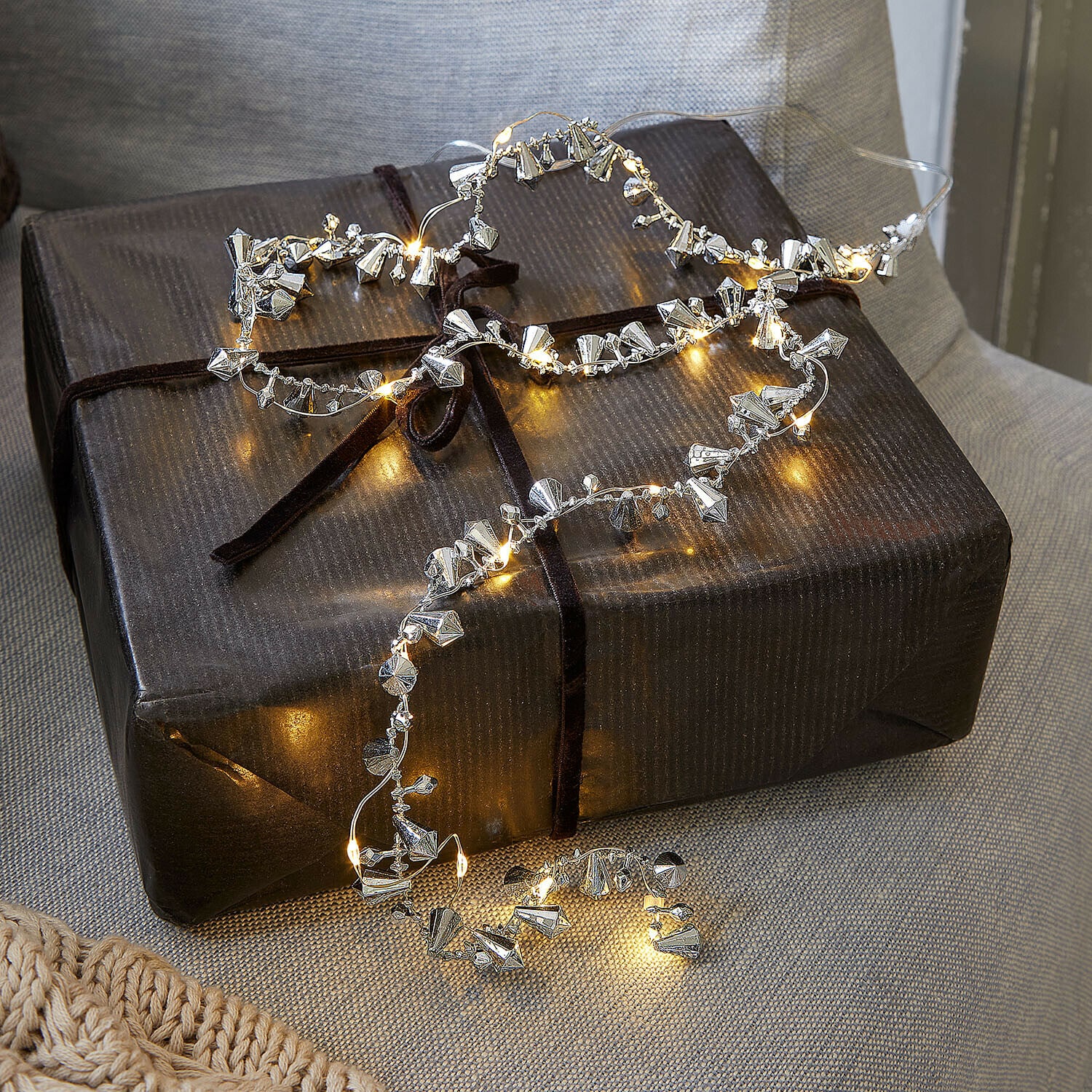 Luces de hadas Bryesa Cadena de luces delicada con adornos metálicos plateados sobre un paquete de regalo oscuro