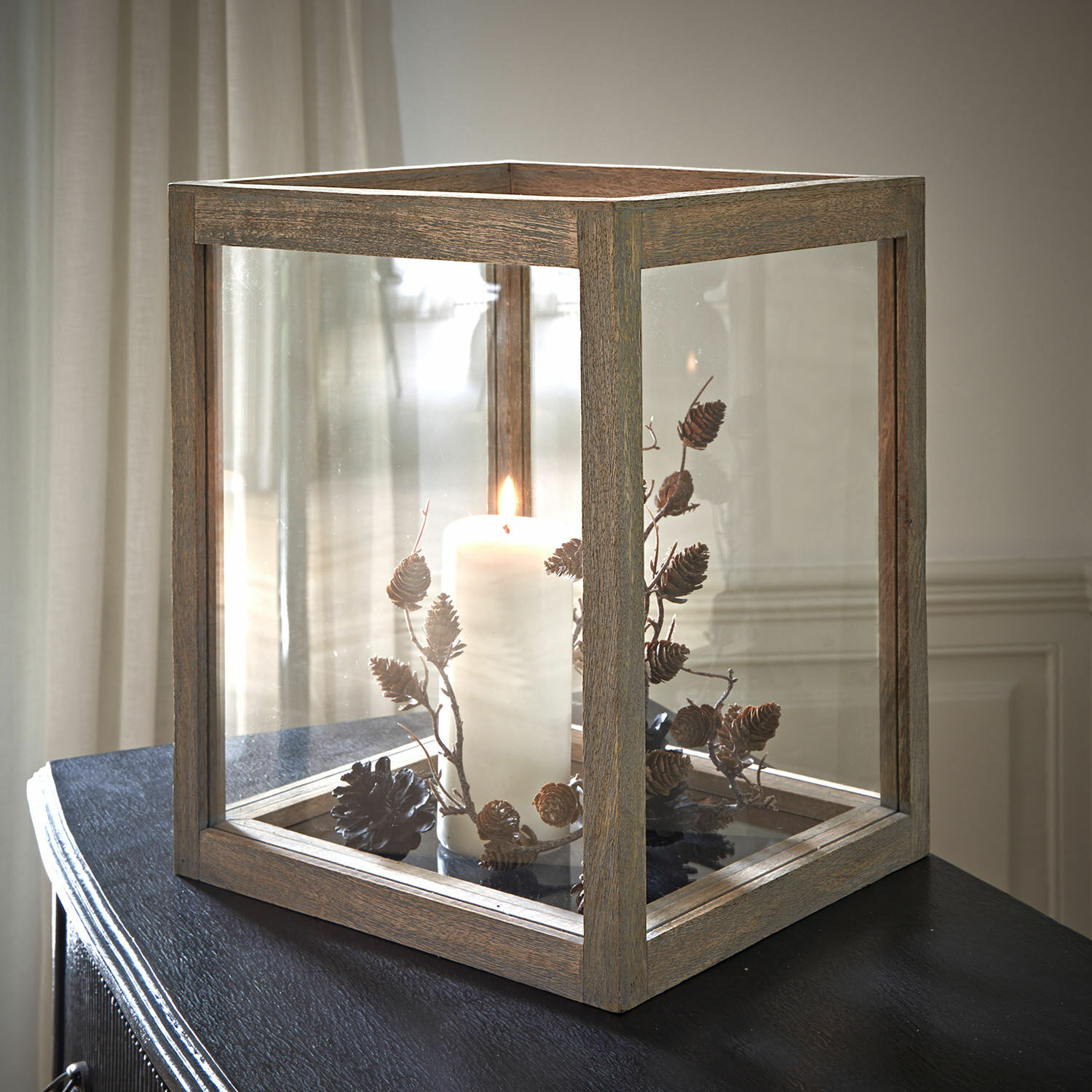 Portavelas Solvik Linterna de madera con cristal transparente y vela blanca decorada con piñas sobre superficie negra