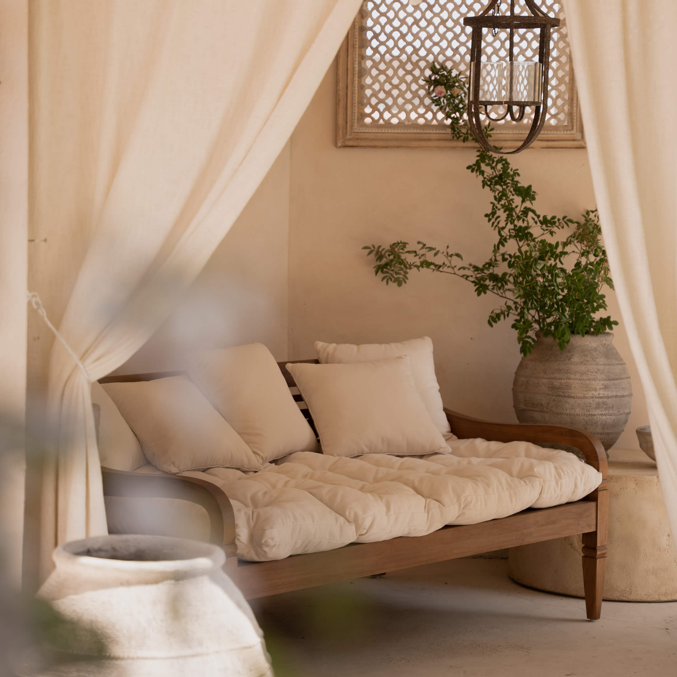 Sofá de madera con cojines crema y colchón suave en un ambiente natural y acogedor