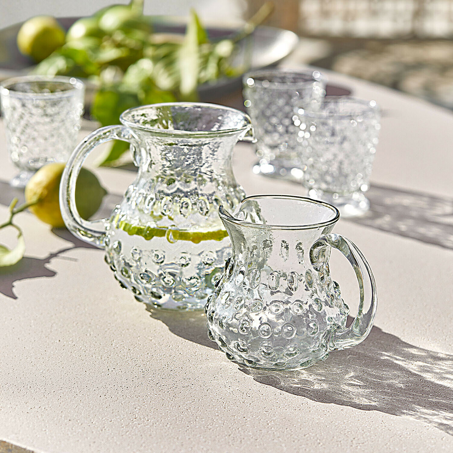 Jarra y jarrita de vidrio con diseño en relieve sobre mesa clara, perfectas para bebidas frescas