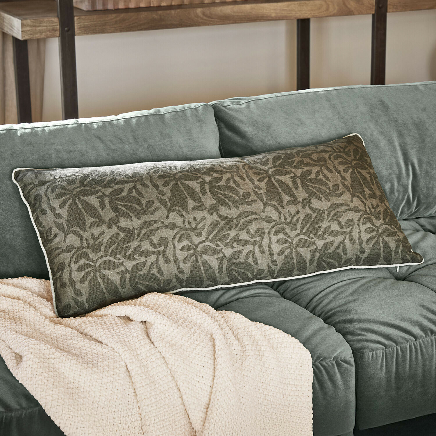 Cojín Rosamound Cojín decorativo alargado verde con patrón floral sobre sofá verde suave con manta beige