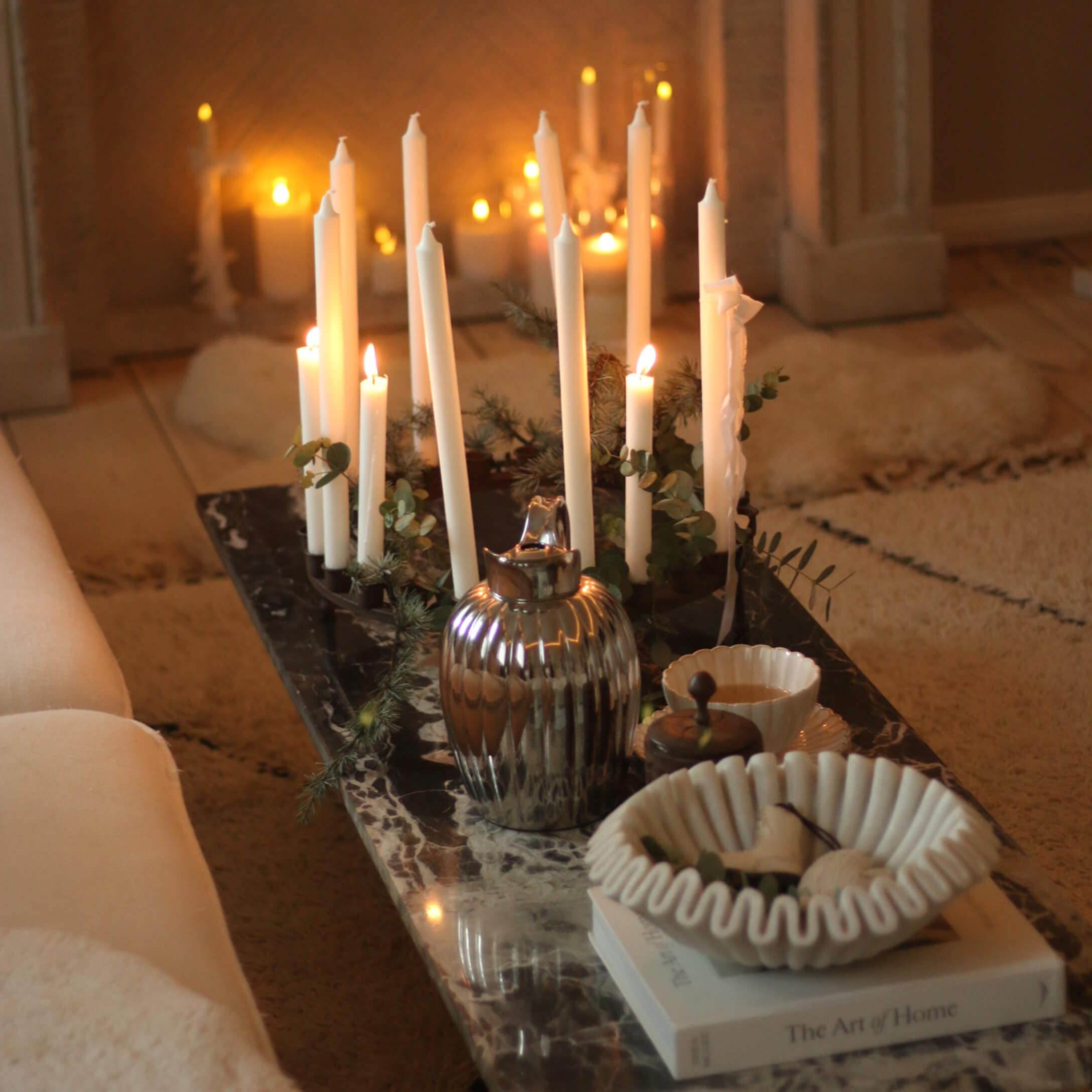 Candelabro decorativo con velas blancas sobre mesa de mármol con cuenco de cerámica y jarra metálica