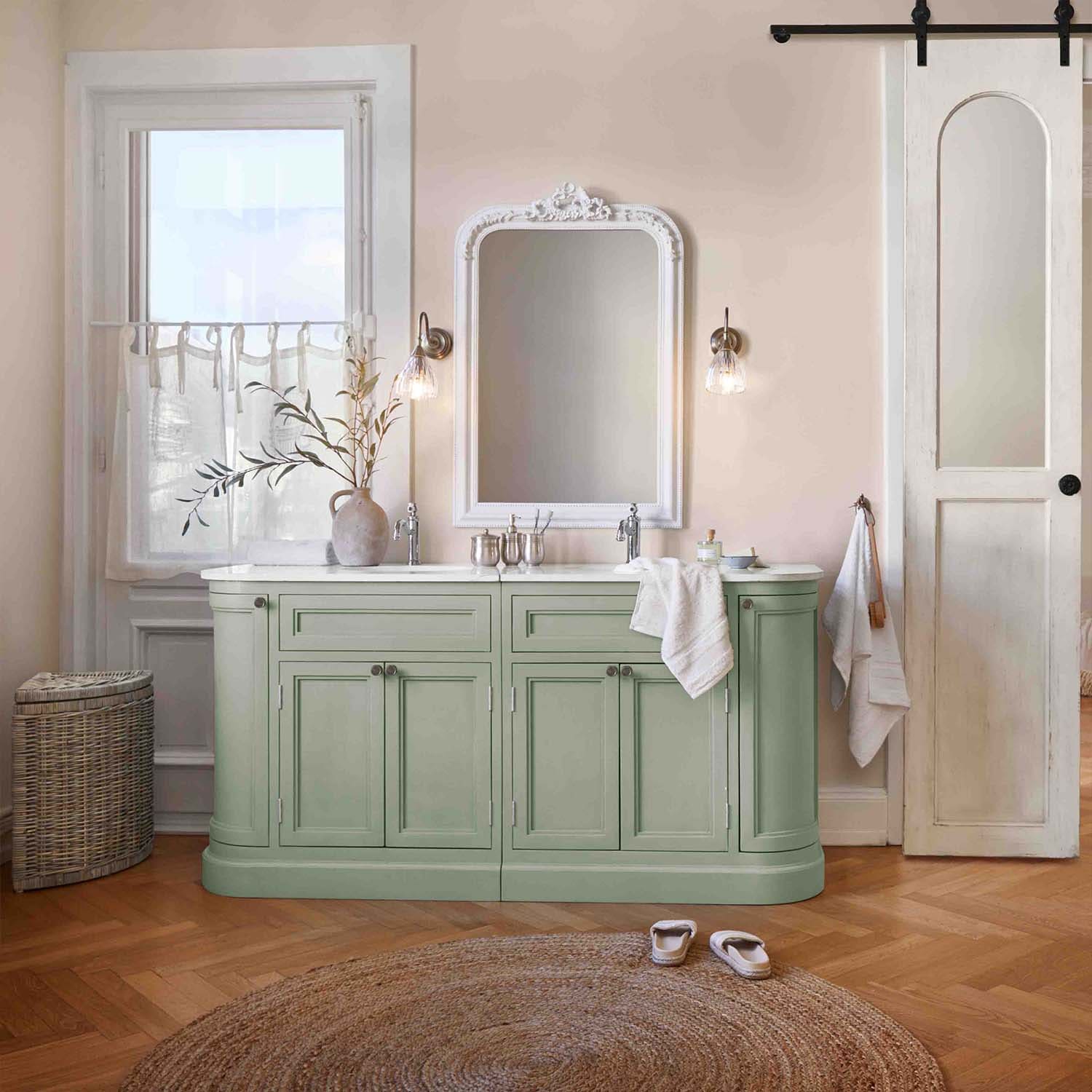 Mueble de baño verde con encimera blanca y espejo vintage en ambiente natural y suave