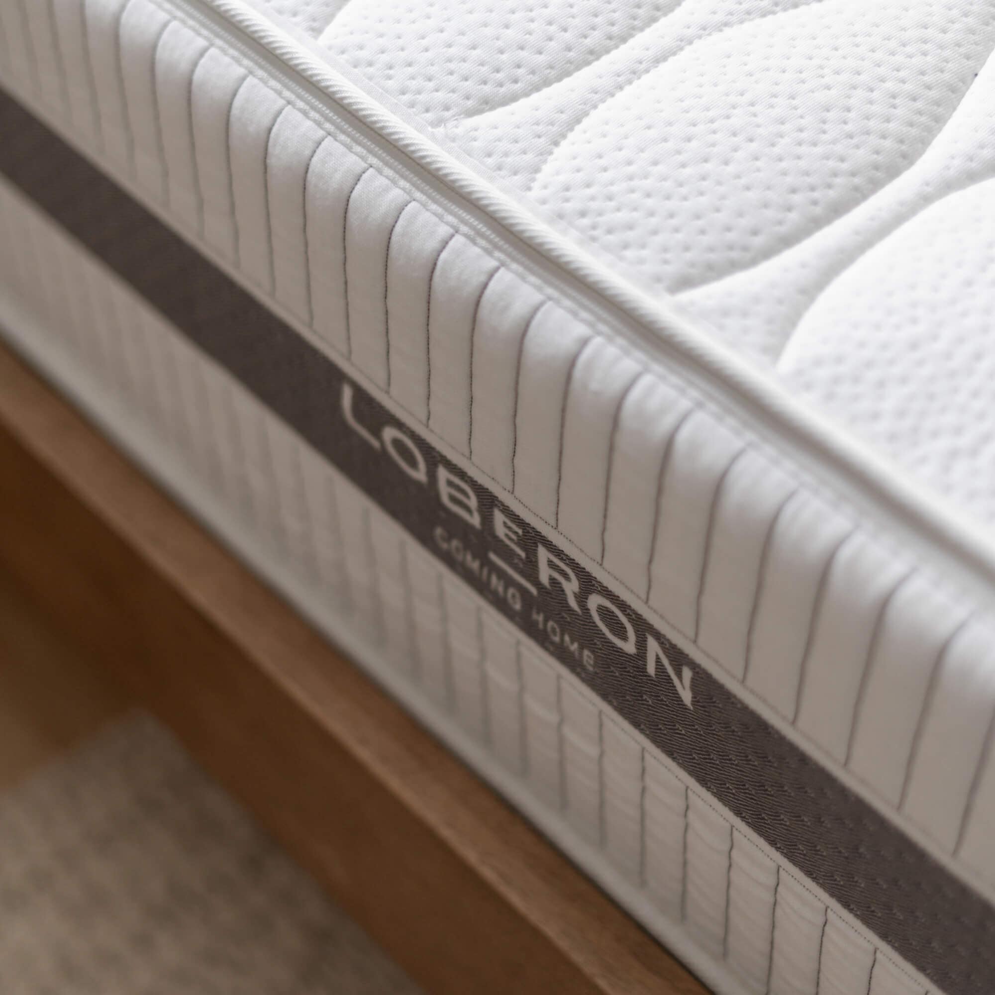 Tela acolchada blanca de colchón con borde gris sobre estructura de cama de madera