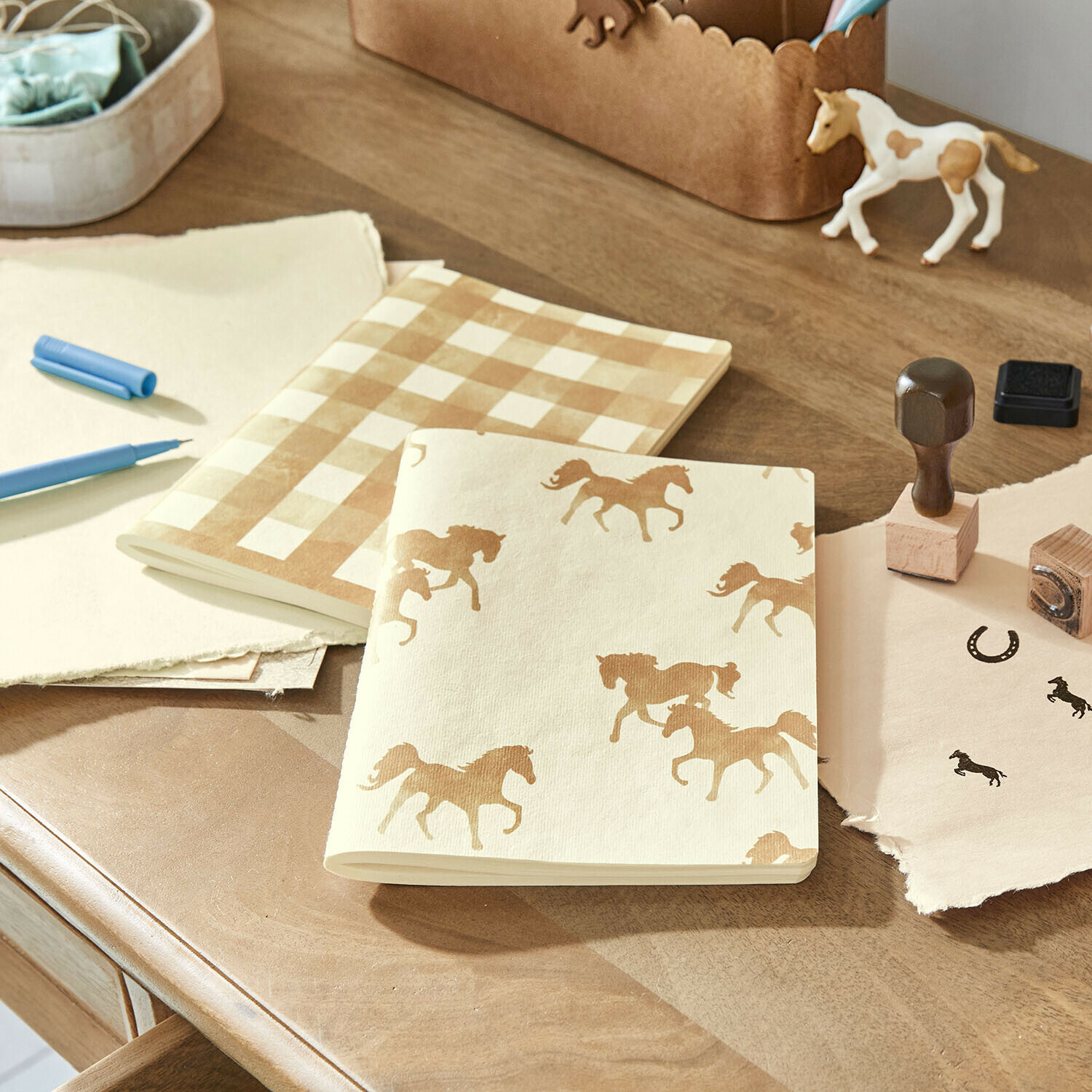 Cuadernos de papel crema con estampado de caballos y cuadros sobre mesa de madera con sellos