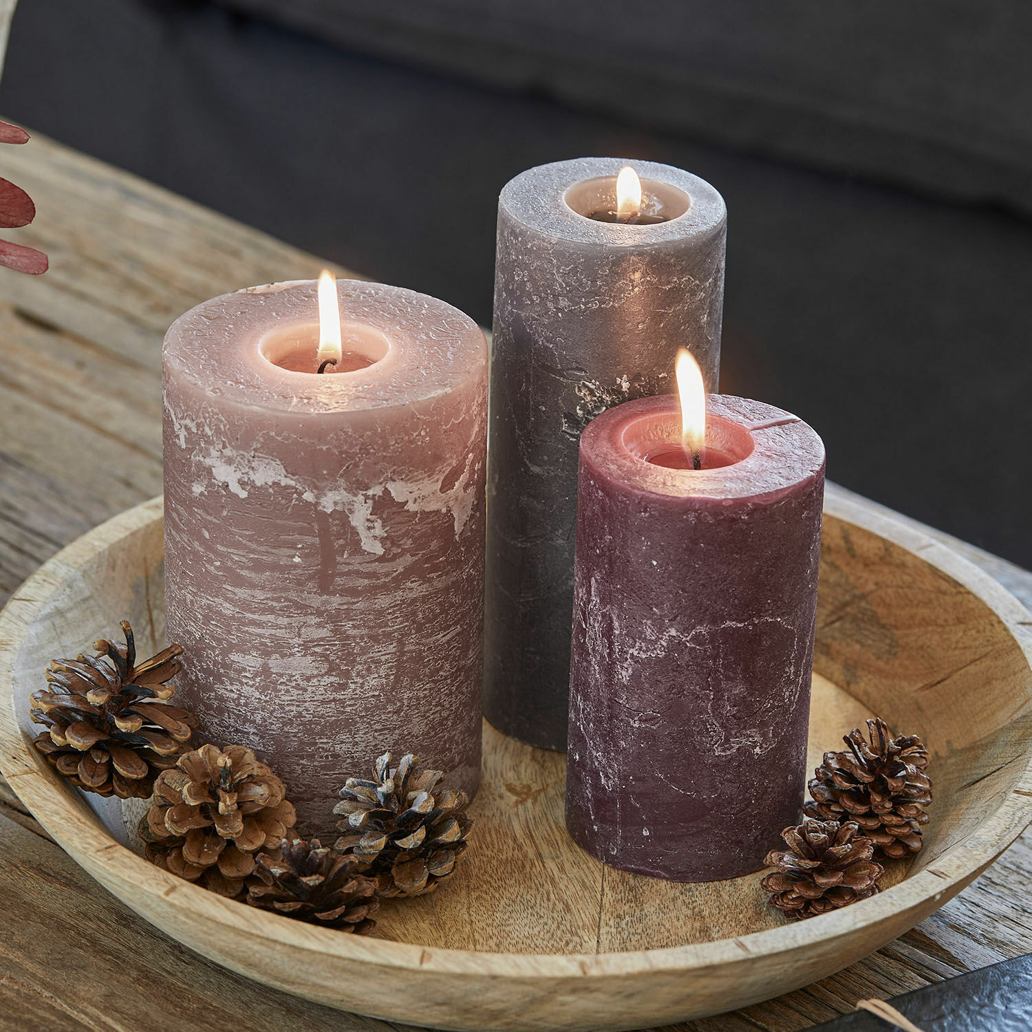 Set de 3 velas Pretin Tres velas encendidas en tonos rosa y gris sobre bandeja de madera con piñas decorativas