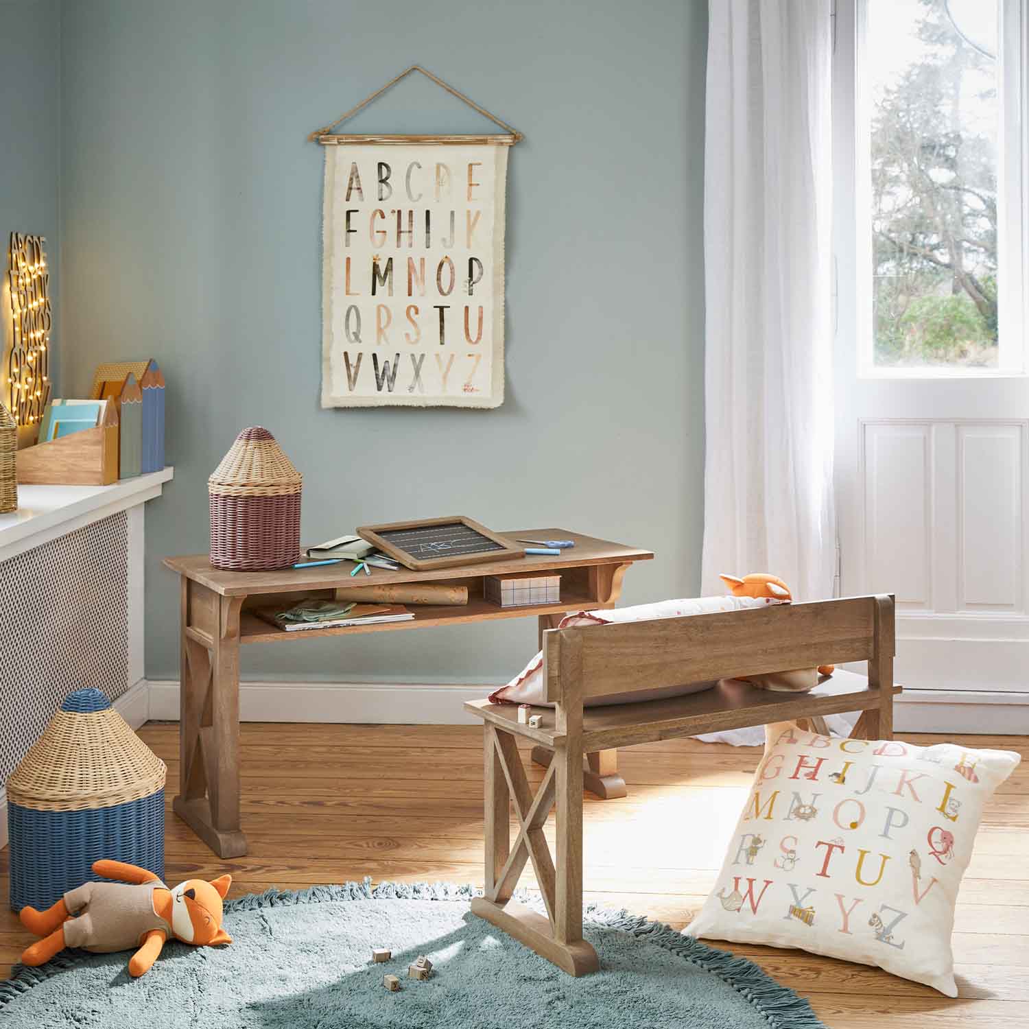Escritorio y banco de madera en habitación infantil con cojín y decoración de alfabeto en la pared