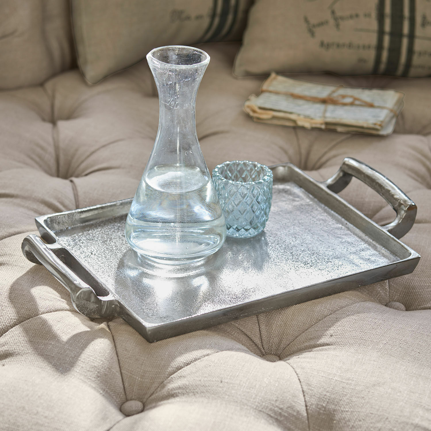 Bandeja Connaire Bandeja decorativa de metal plateado sobre tela beige acolchada con jarra y vaso de cristal