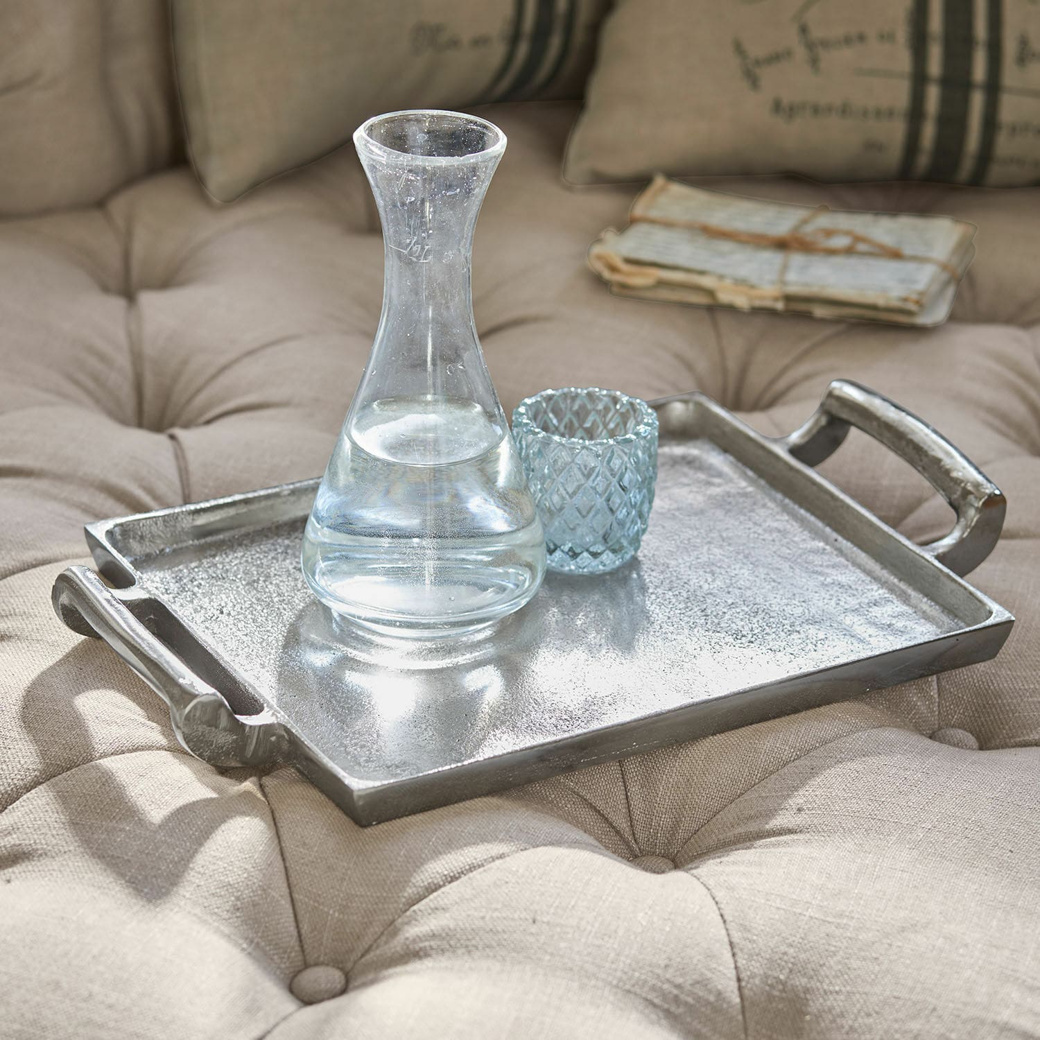 Bandeja Connaire Bandeja decorativa de metal plateado sobre tela beige acolchada con jarra y vaso de cristal