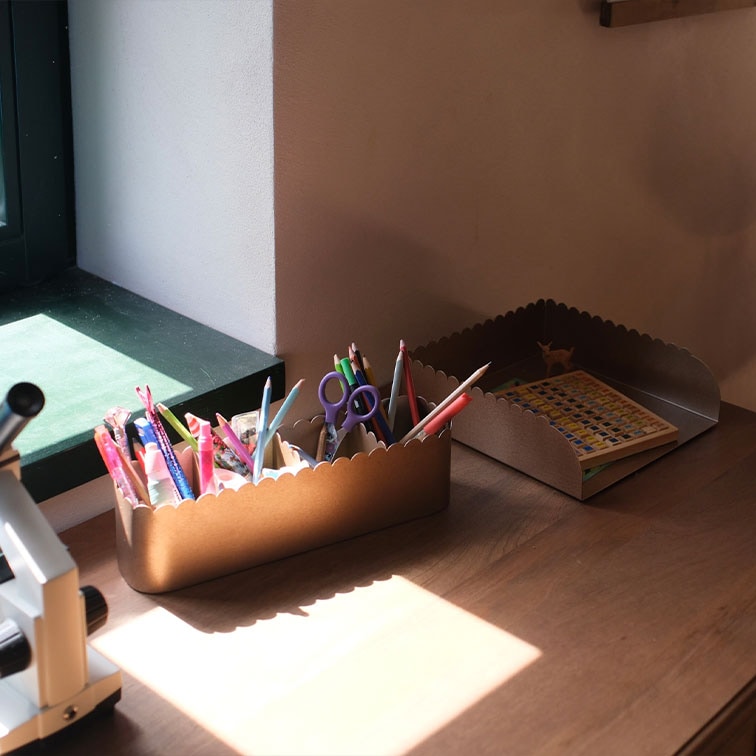 Organizadores de metal marrón con bordes ondulados, llenos de útiles de escritura y un libro