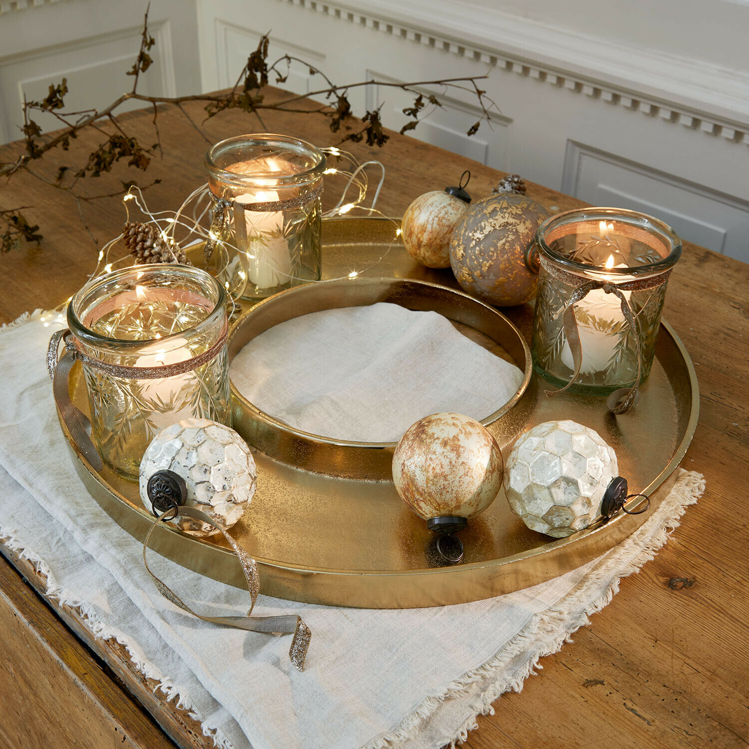 Bandeja para velas Velarosas Bandeja metálica dorada con tres portavelas de cristal y bolas decorativas sobre mesa de madera