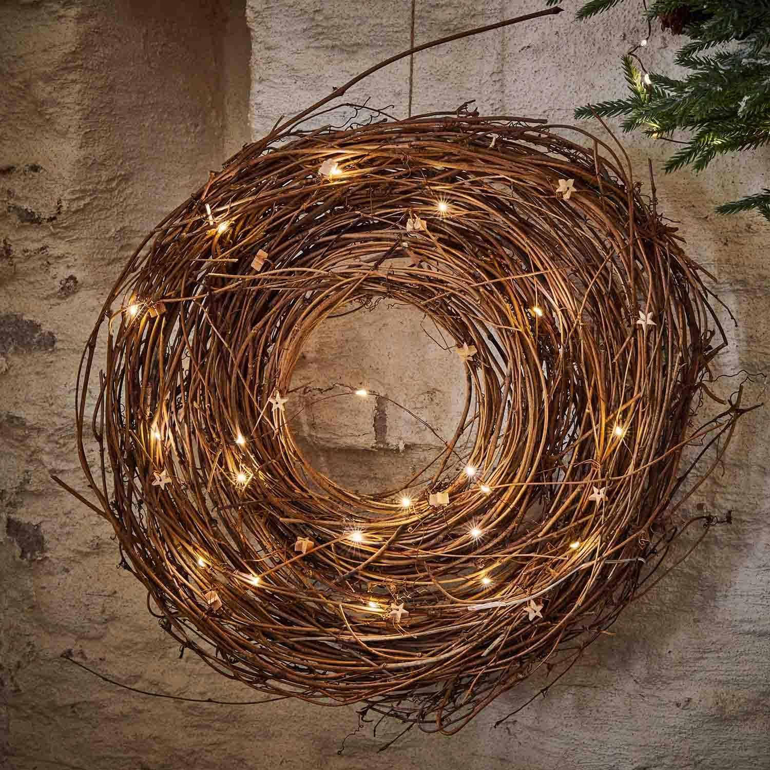Corona decorativa de ramas naturales con luces LED suaves colgada en la pared