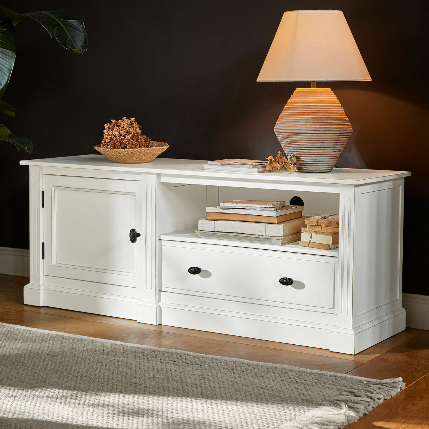 Aparador blanco de madera con cajón y puerta, lámpara decorativa y libros encima