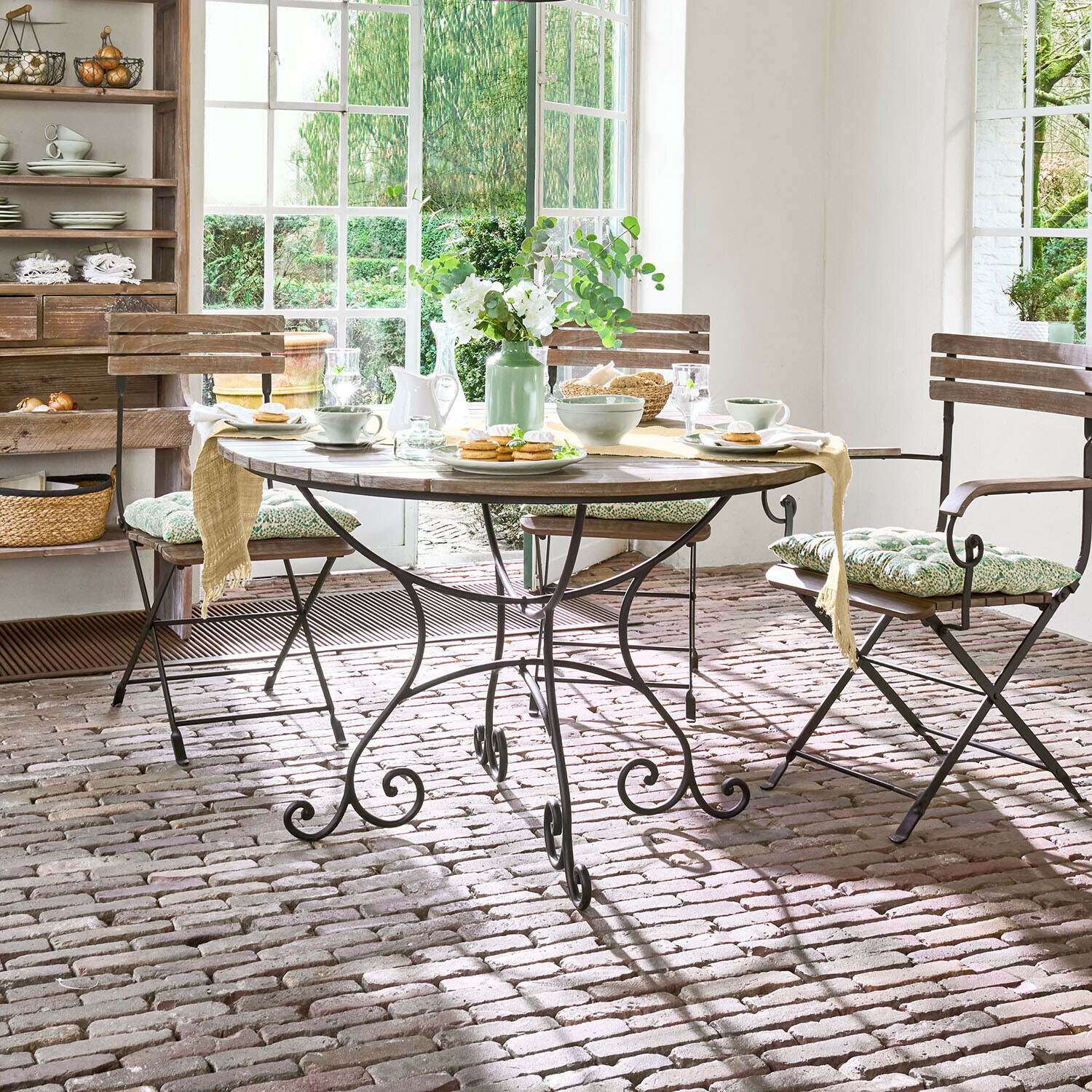 Mesa Arémont Mesa redonda de madera con base metálica en comedor rústico con sillas y decoración floral