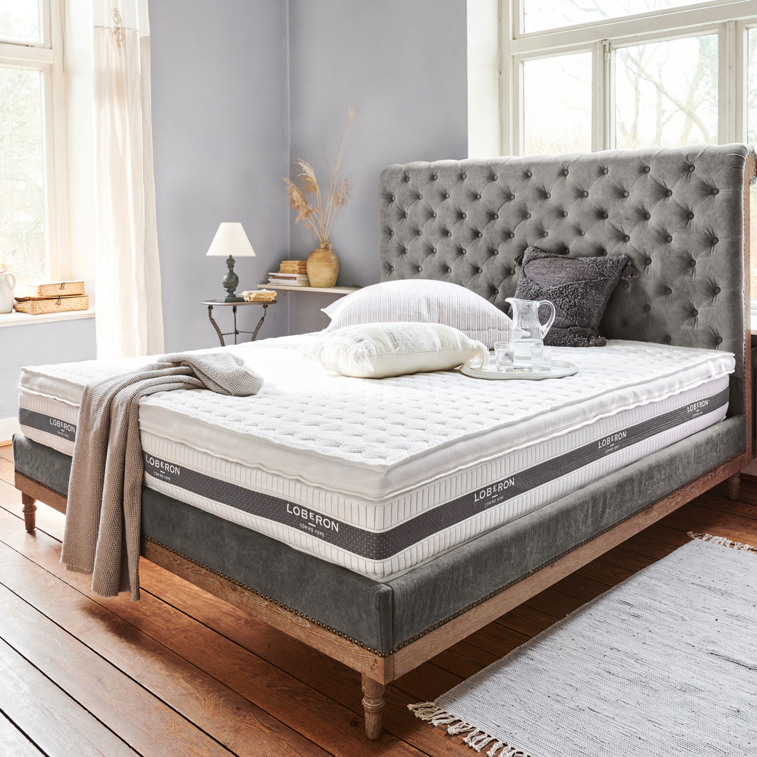 Topper Danisar Cama con cabecero gris acolchado y colchón blanco Loberon en habitación luminosa y acogedora