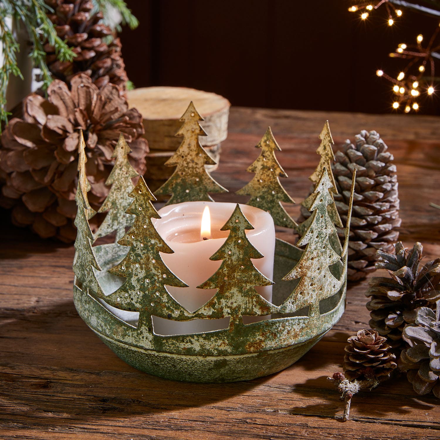 Portavelas metálico con diseño de árboles de Navidad en verde oxidado con vela blanca sobre mesa de madera