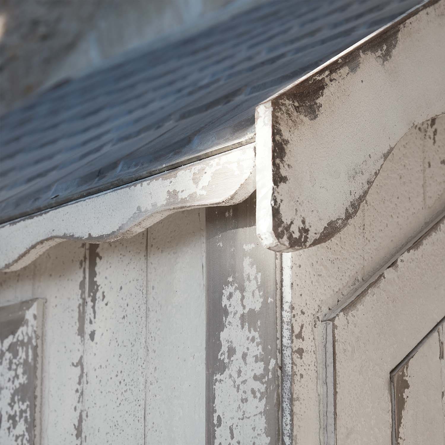 Primer plano de estructura de madera blanca envejecida con techo metálico y borde curvado