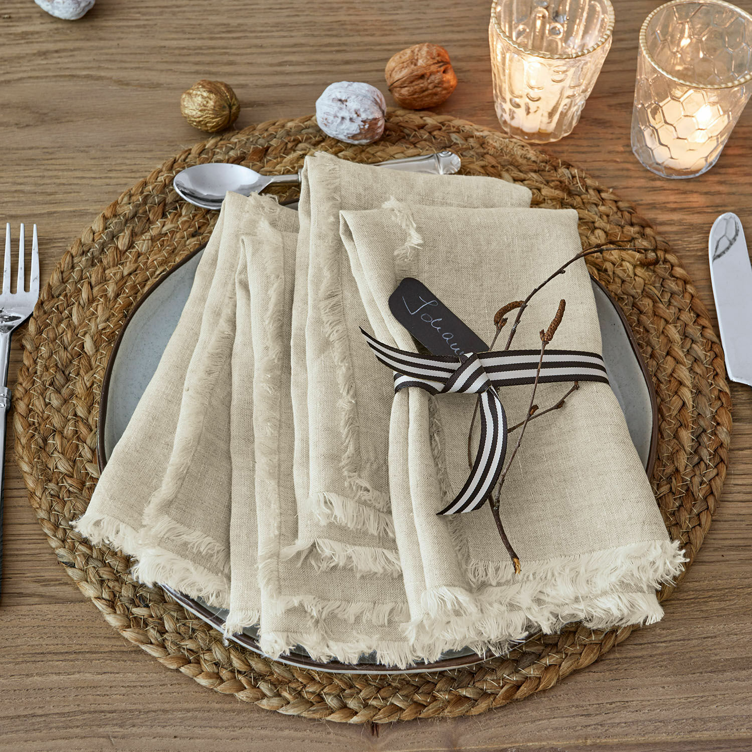 Set de 4 servilletas Largo Servilletas de lino beige con flecos sobre un salvamanteles trenzado de madera con decoración navideña