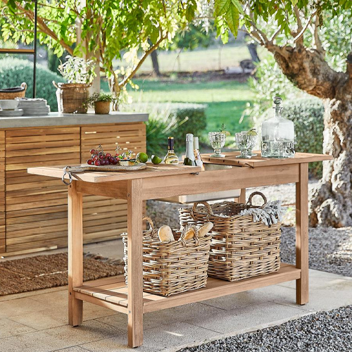 Mesa de jardín de madera natural con cestas de mimbre y accesorios para servir en terraza soleada