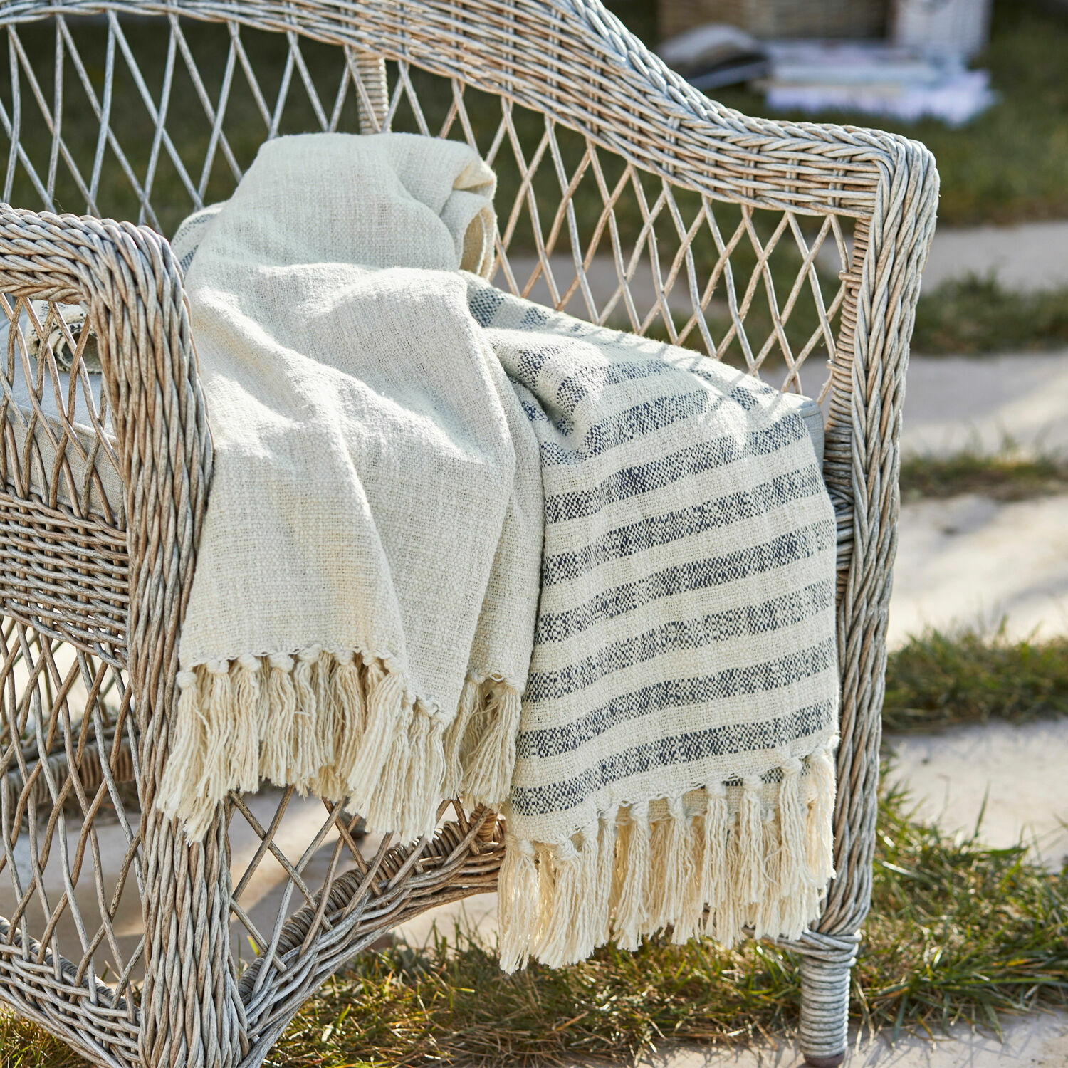 Plaid Marpent Manta beige de algodón con flecos sobre silla de mimbre en jardín, decoración y confort
