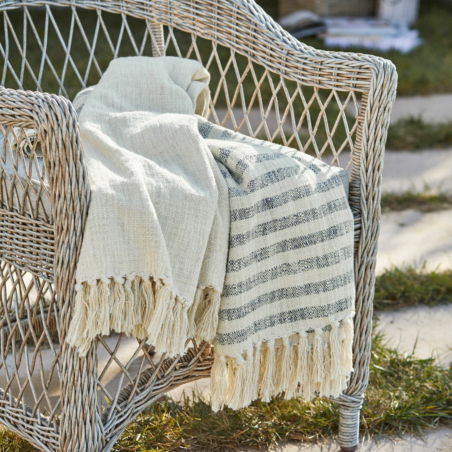Plaid Marpent Manta beige de algodón con flecos sobre silla de mimbre en jardín, decoración y confort