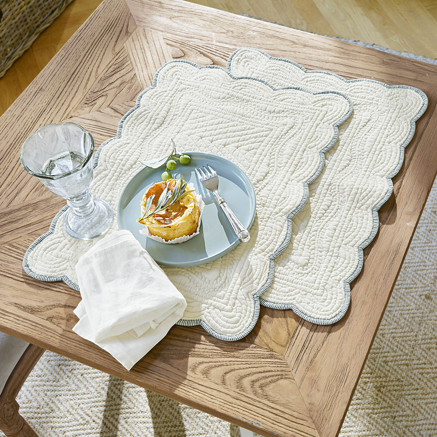 Juego de 2 manteles individuales Fontienne Individuales acolchados de algodón beige con borde azul sobre mesa de madera con postre y vaso