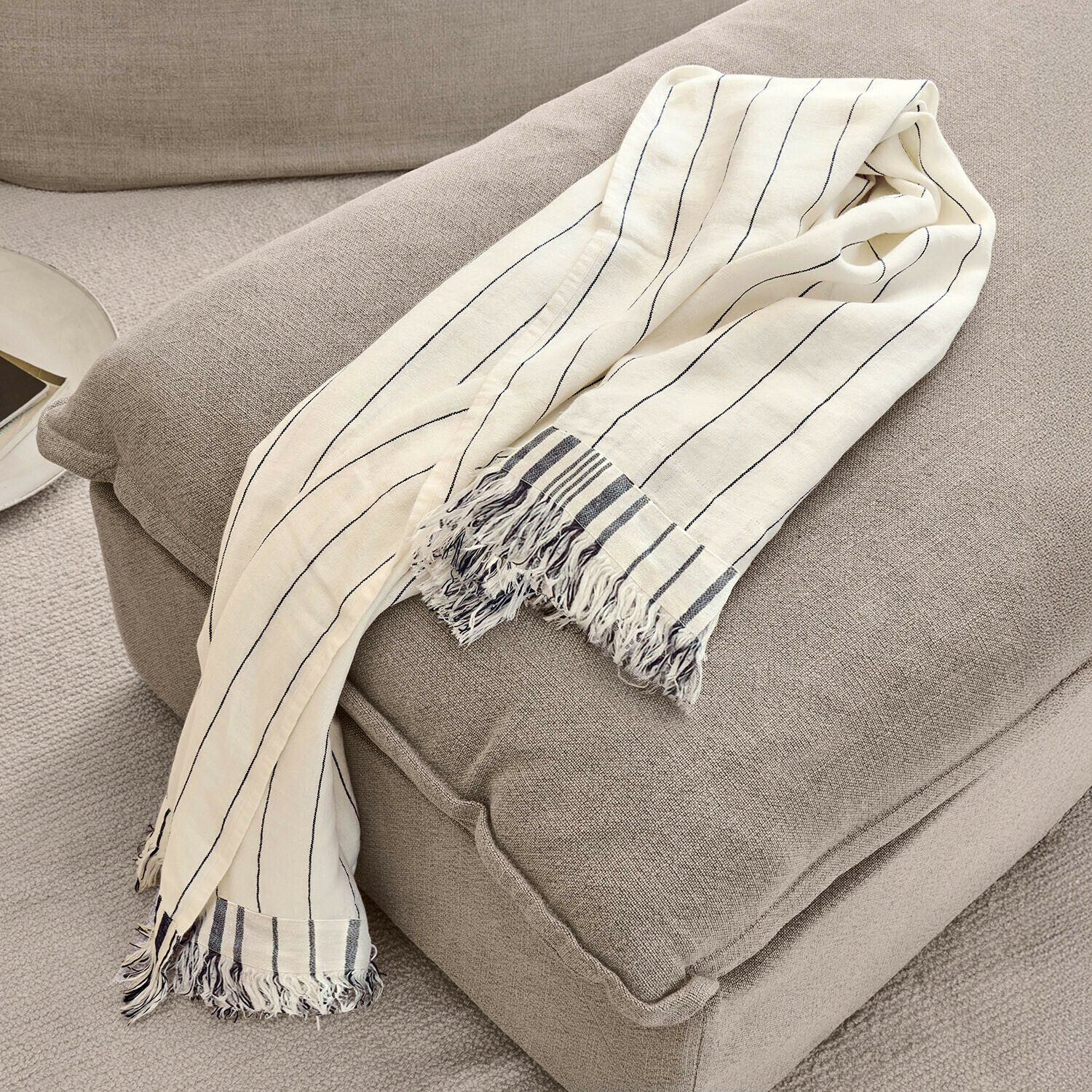 Plaid Ulderina Manta beige de algodón con rayas negras y flecos sobre sillón gris, decoración acogedora para el hogar