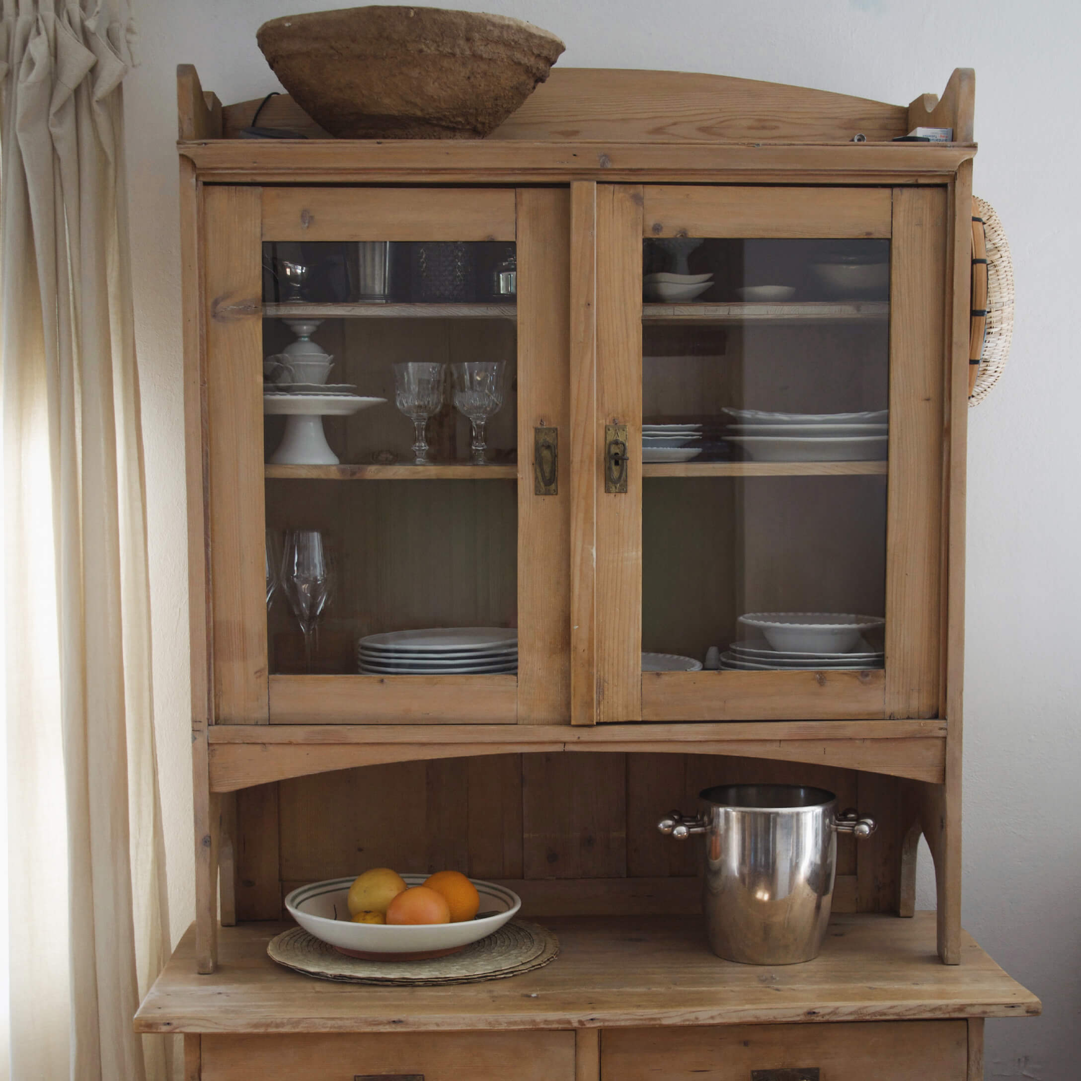 Aparador de madera con puertas de cristal, vajilla blanca y cubo metálico en la encimera