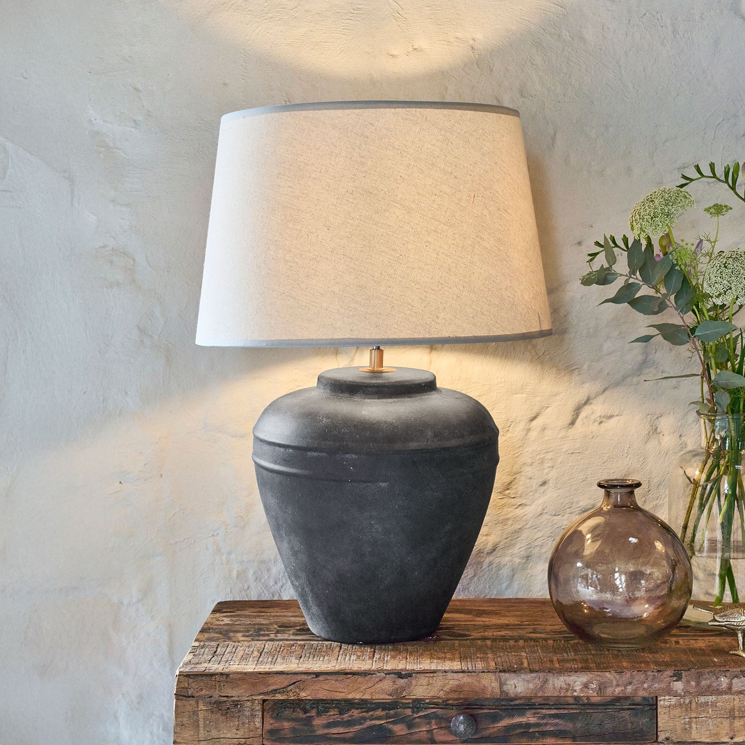 Lámpara de mesa de cerámica negra con pantalla beige sobre mesa de madera rústica