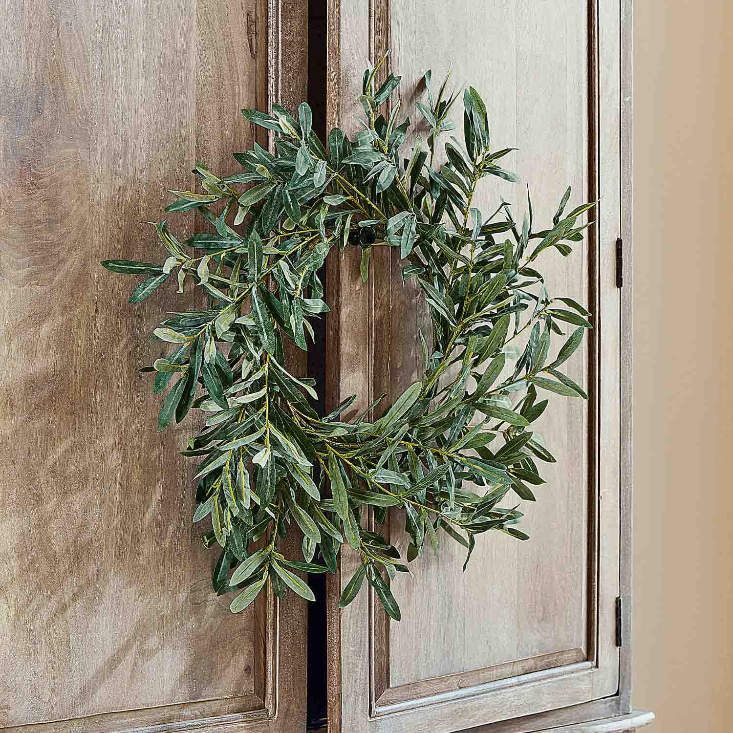 Corona decorativa de hojas verdes colgada en puerta de madera, decoración natural para interiores