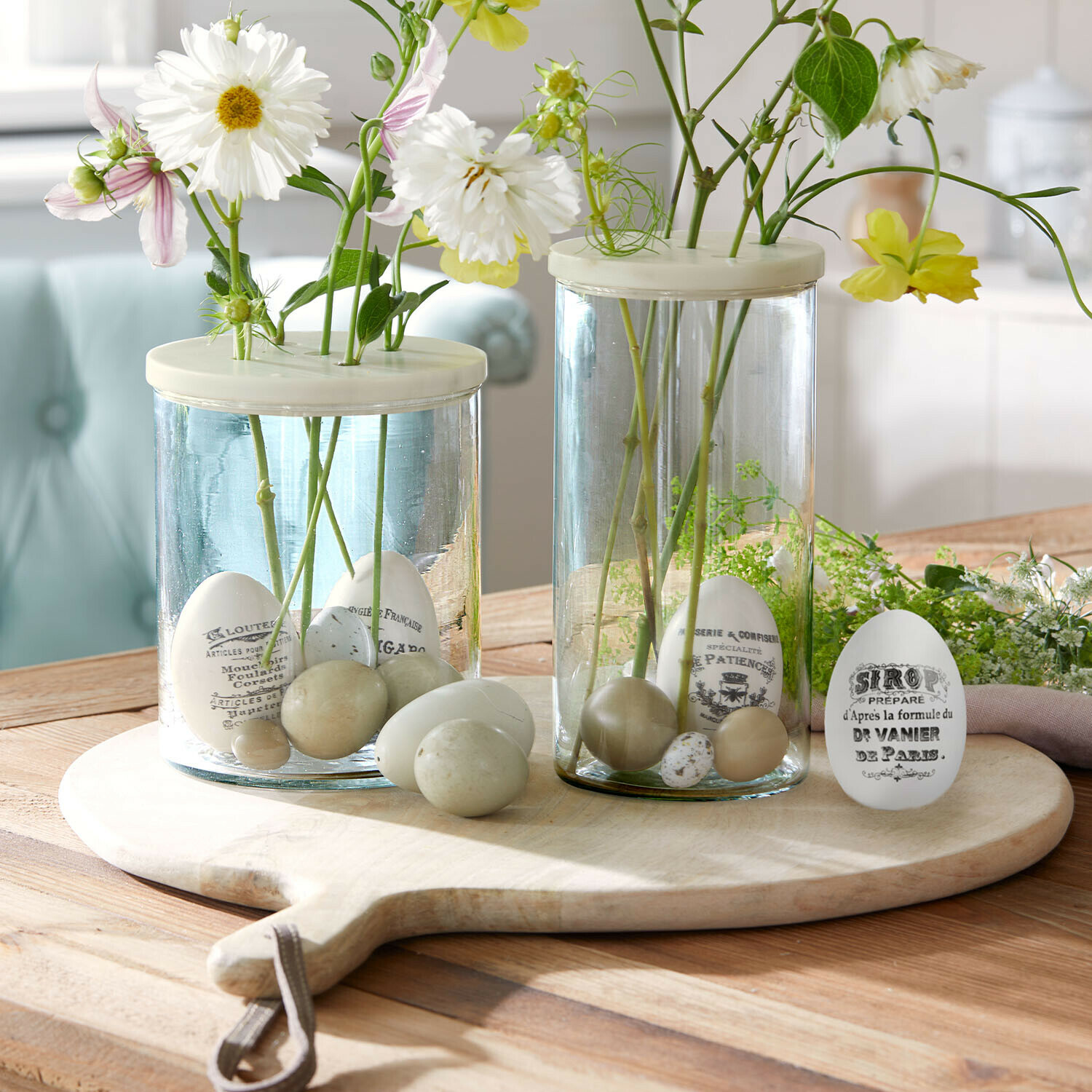 Set de 4 huevos de Pascua Maison Vélour Jarrones de vidrio con huevos decorativos blancos y beige y flores sobre tabla de madera