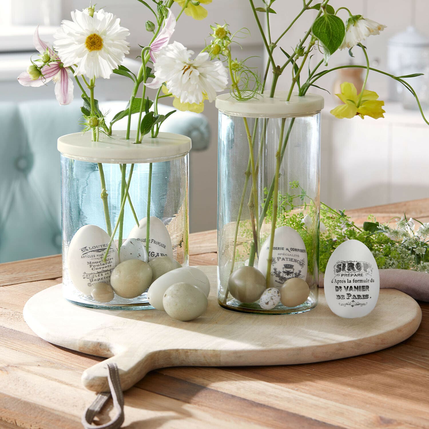 Set de 4 huevos de Pascua Maison Vélour Jarrones de vidrio con huevos decorativos blancos y beige y flores sobre tabla de madera