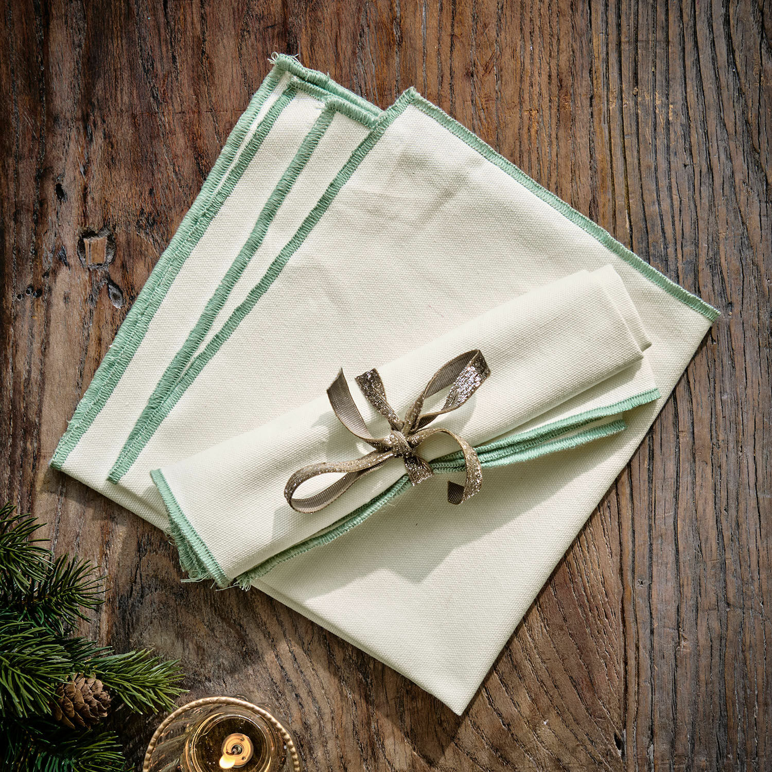 Set de 2 servilletas Tarivelle Juego de servilletas de lino crema con borde verde sobre mesa de madera, decoración navideña