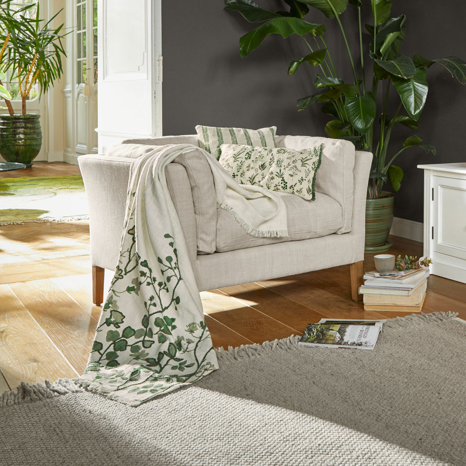 Sofá beige de tela con cojines verdes y manta decorativa con diseño vegetal en sala de estar