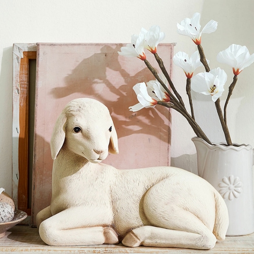 Figura decorativa de cordero claro junto a un jarrón con flores blancas, adorno para interiores
