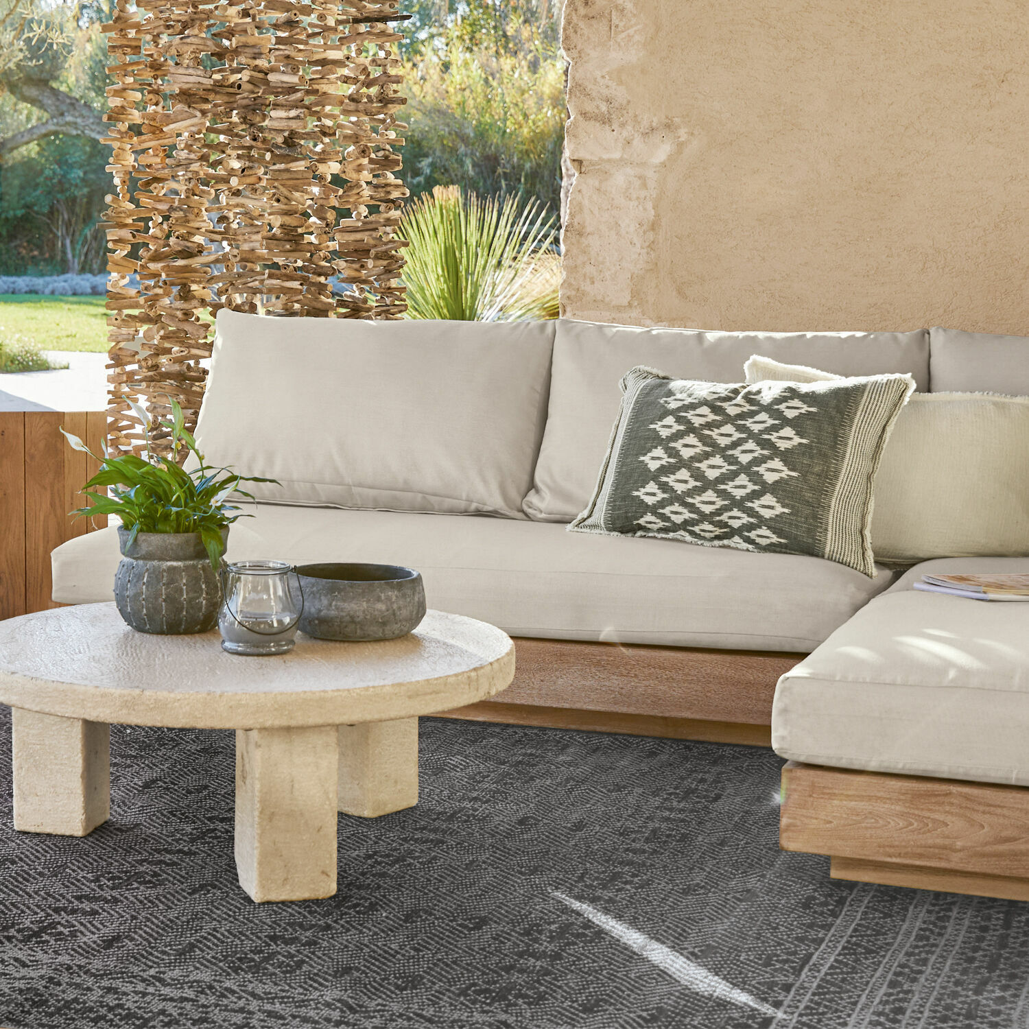 Sofaelement Courtelevant Sofá beige con base de madera y cojín decorativo sobre alfombra negra en sala luminosa.