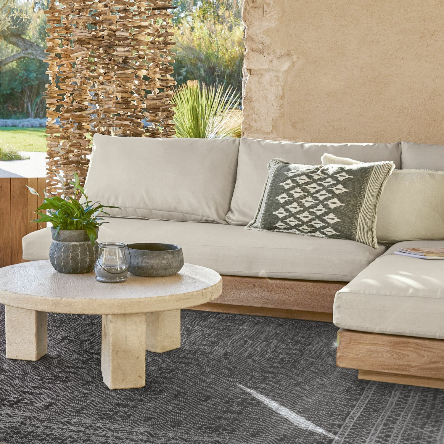 Sofaelement Courtelevant Sofá beige con base de madera y cojín decorativo sobre alfombra negra en sala luminosa.