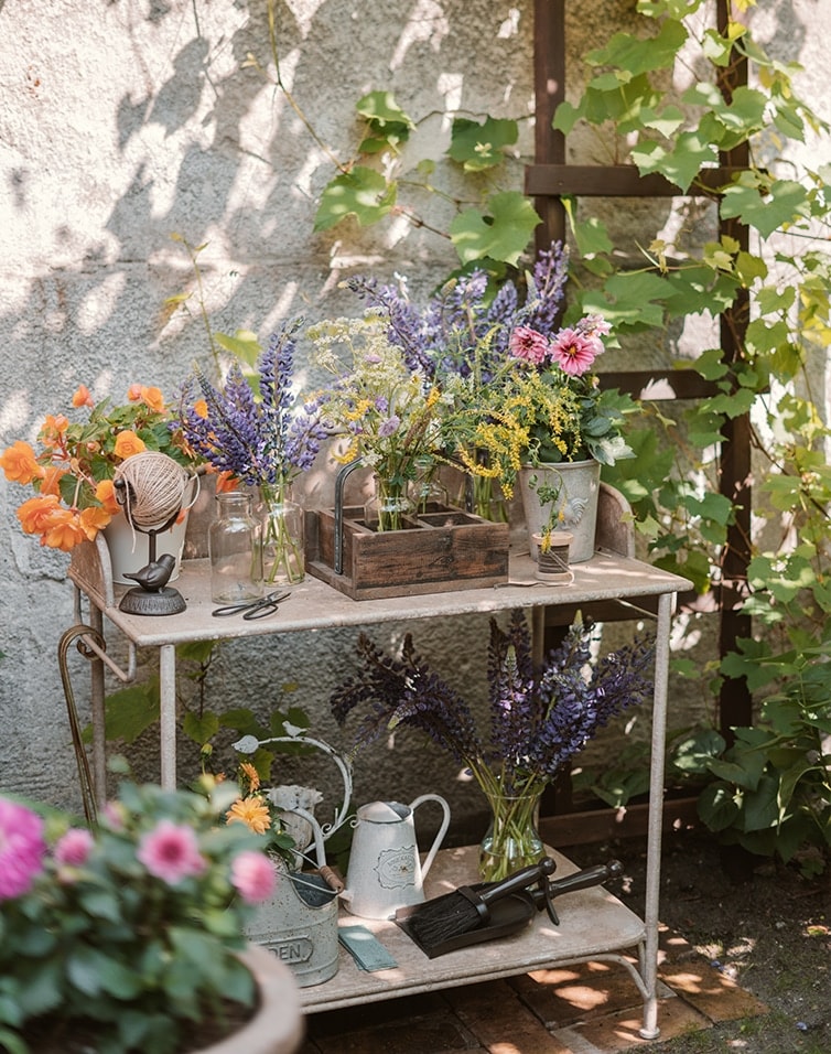 Mesa de jardín de metal con flores y herramientas de jardinería en un lugar soleado y sombreado