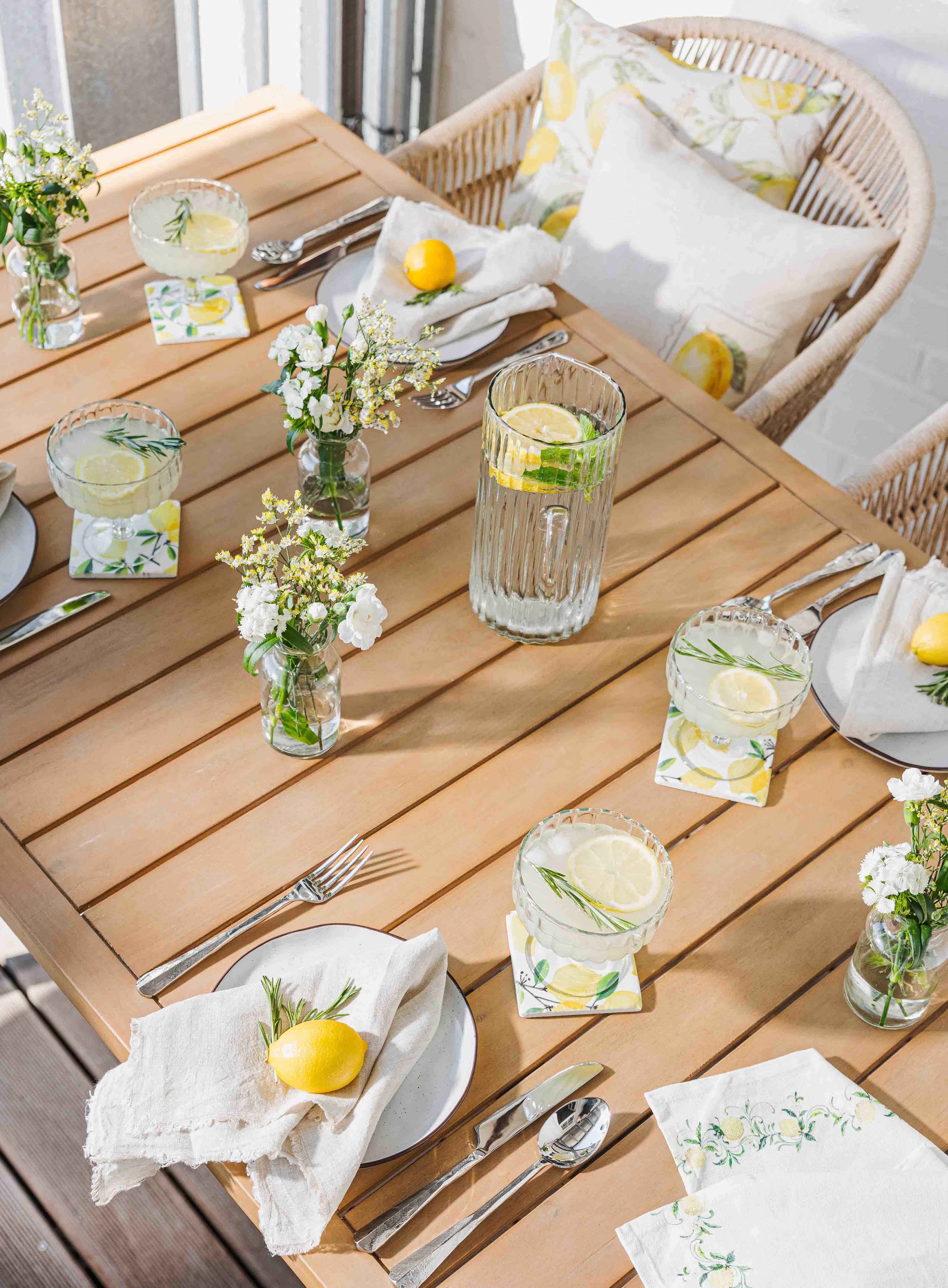 Mesa de madera clara con limonada, vasos y decoración de limón para ambiente veraniego en jardín