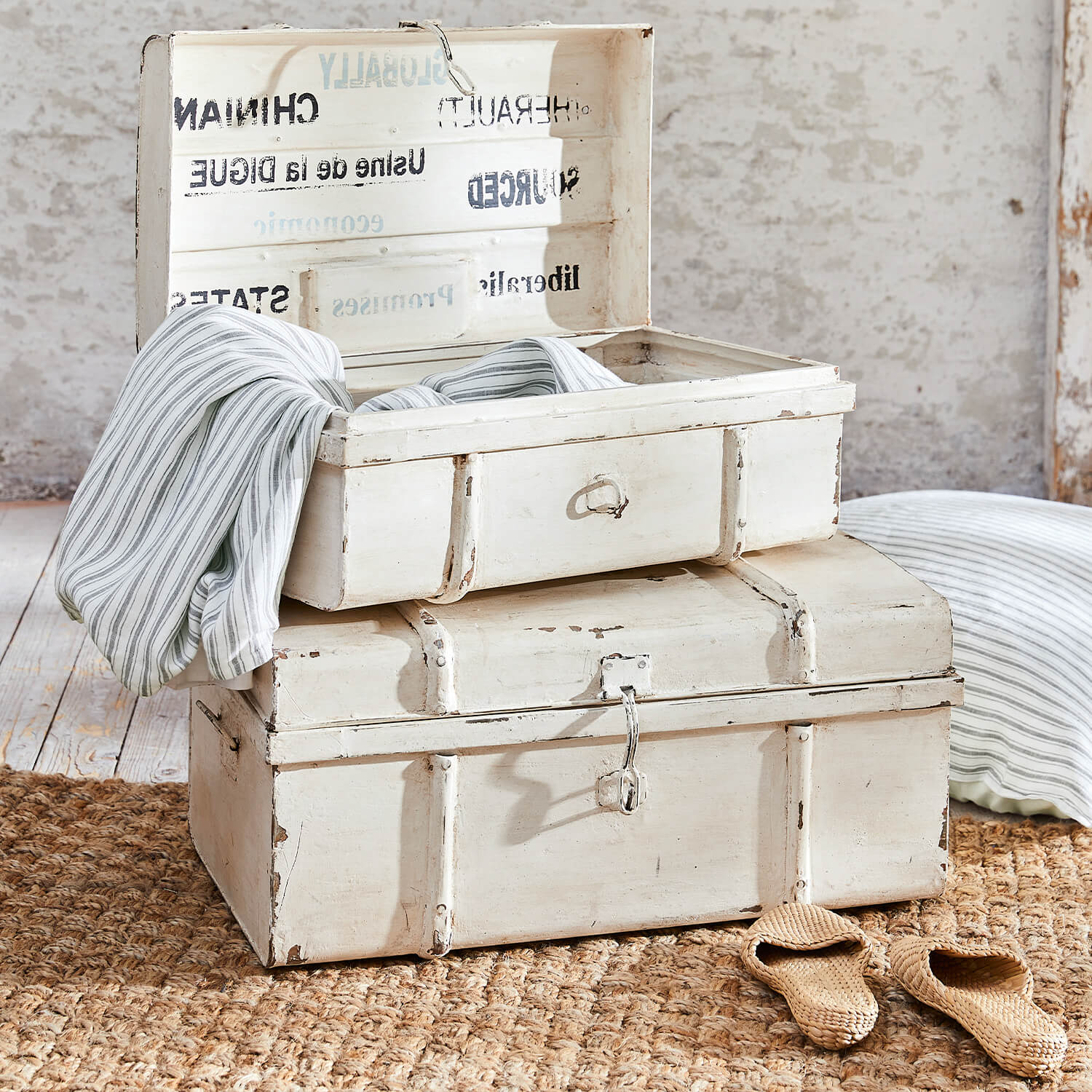 Cajas de madera blancas envejecidas sobre alfombra de yute con tela a rayas dentro