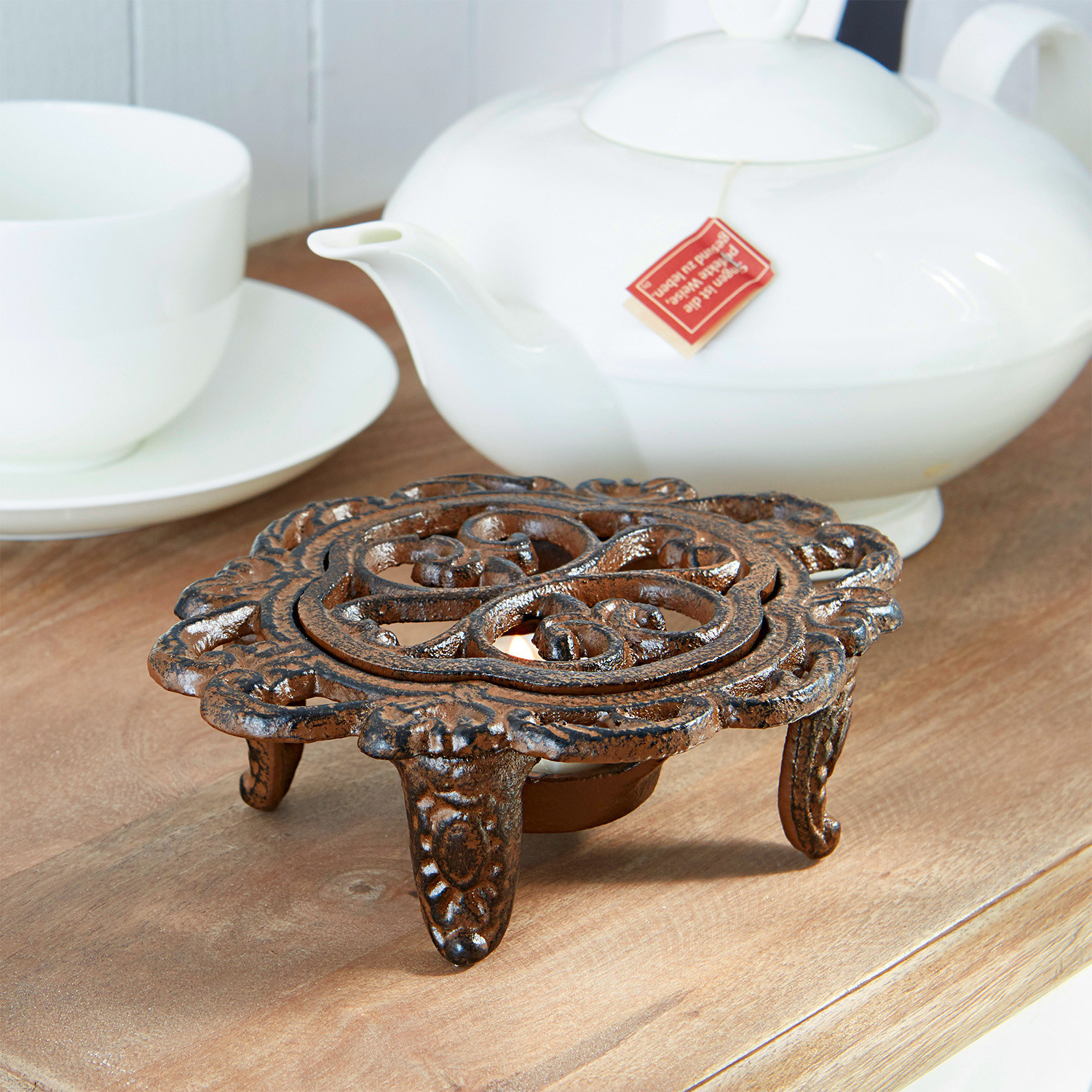 Calentador de tetera Florian Calentador de té decorativo de hierro fundido marrón sobre mesa de madera con porcelana blanca