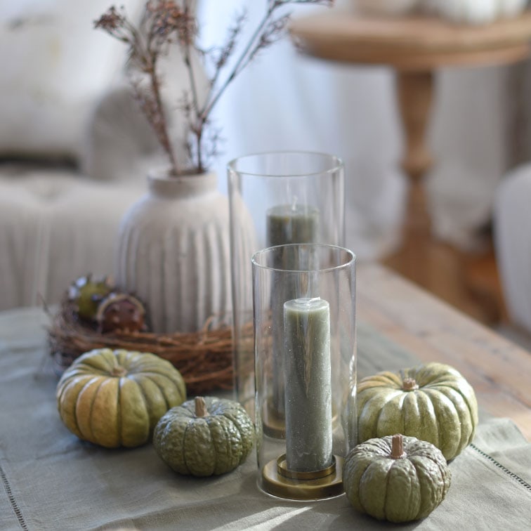 Velas verdes decorativas y calabazas en portavelas de vidrio sobre mesa de madera en estilo natural