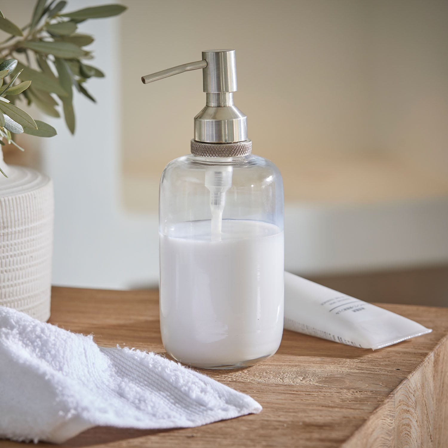 Dispensador de jabón transparente de acero inoxidable con líquido blanco sobre superficie de madera