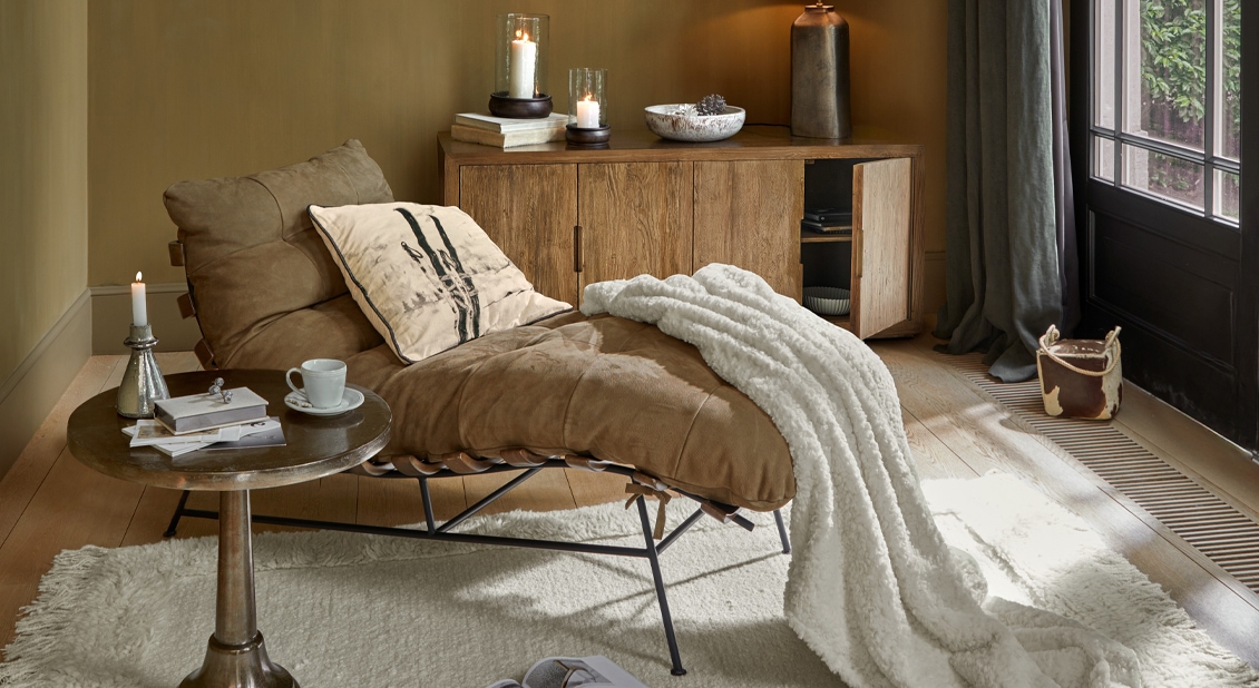 Sillón marrón con tapizado suave y manta blanca en salón acogedor con aparador de madera y mesa auxiliar