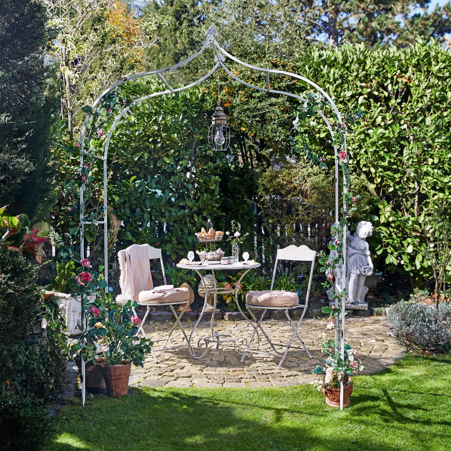 Arco de rosas Dimarus Arco de jardín metálico blanco con flores rosas y lámpara, mesa y sillas en patio de piedra