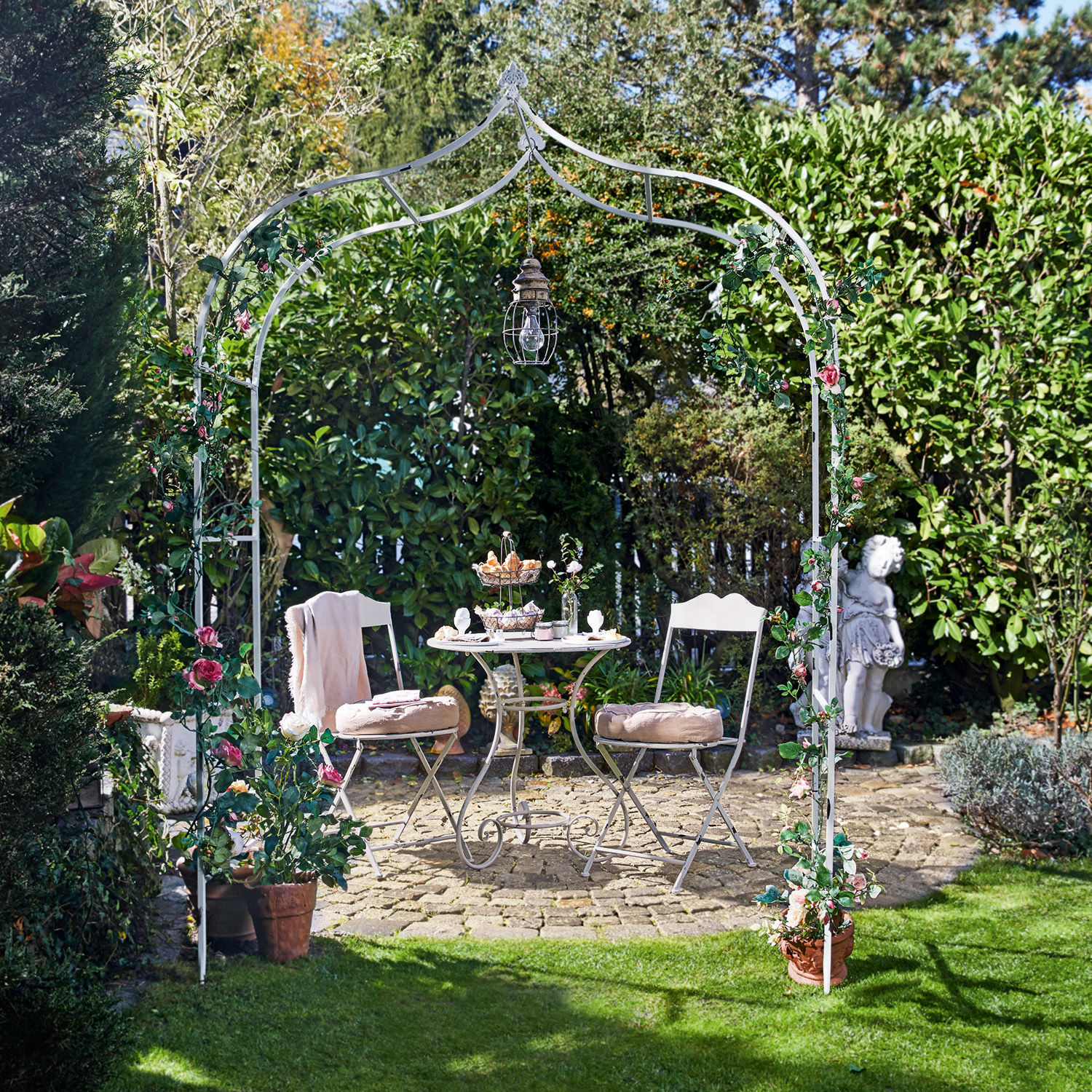 Arco de rosas Dimarus Arco de jardín metálico blanco con flores rosas y lámpara, mesa y sillas en patio de piedra